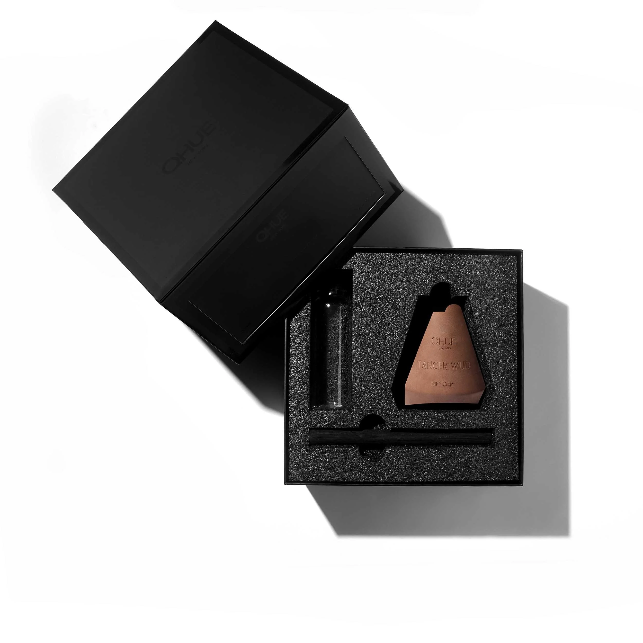 Qhue New York Tanger Wud Volcanic Reed Diffuser gift set featuring a hand-painted brown cement vessel, fragrance refill bottle, and black bamboo reed in a premium black presentation box.