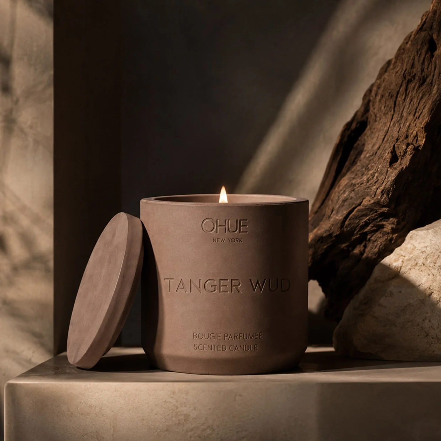 Qhue New York Tanger Wud scented candle in a hand-painted cement vessel with warm architectural lighting and natural wood accents.