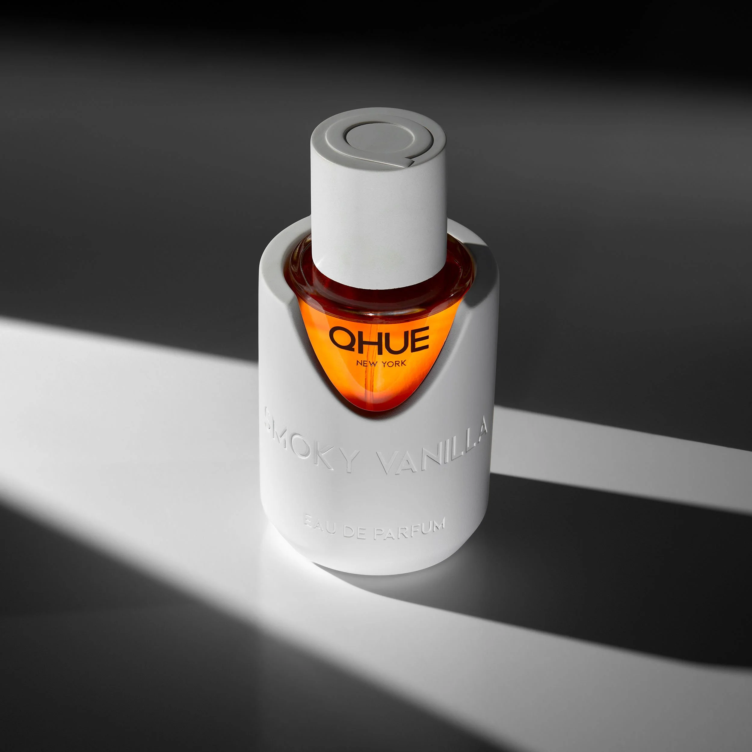 Qhue New York Smoky Vanilla Eau de Parfum in a white architectural bottle with warm amber fragrance illuminated by natural light.