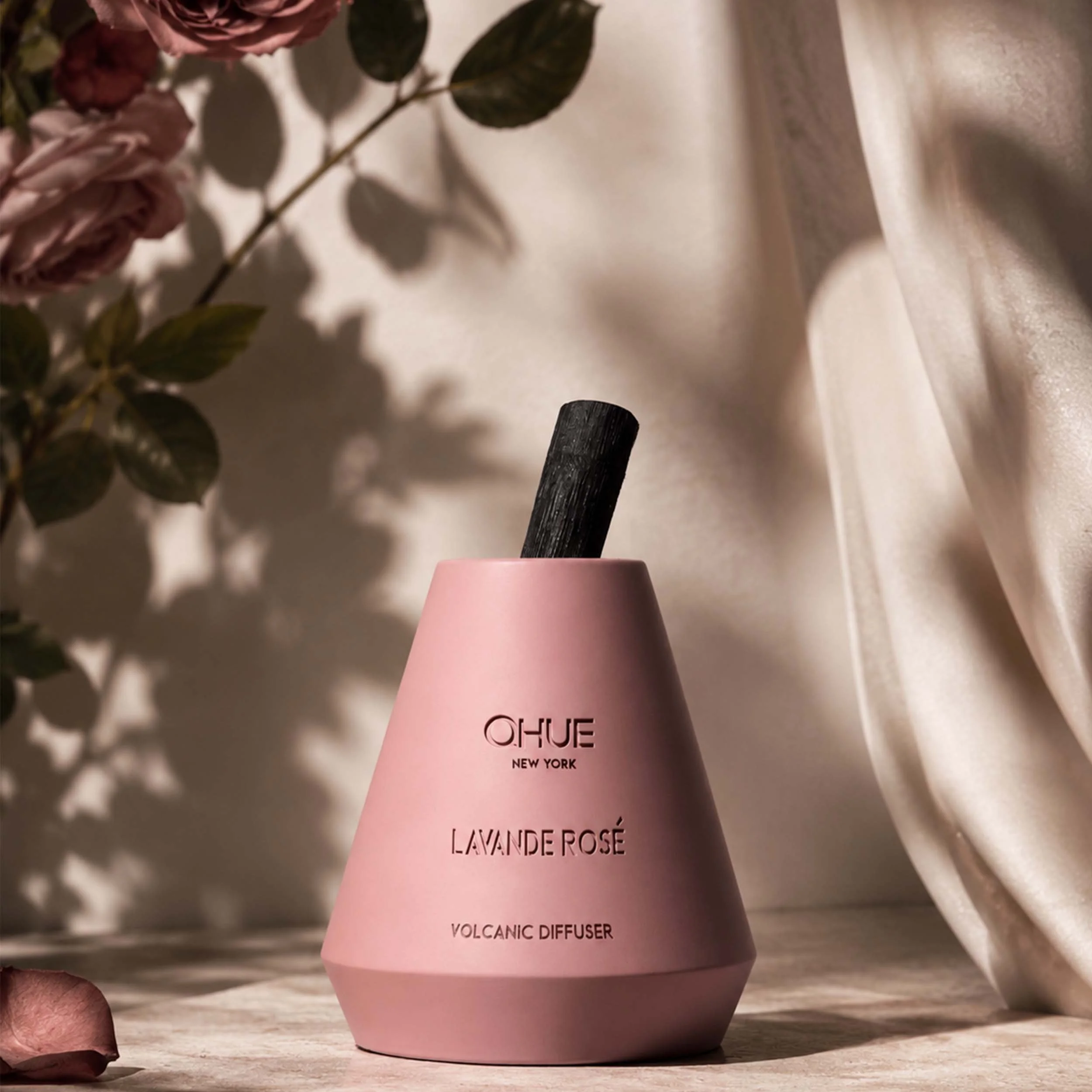 Qhue New York Lavande Rosé Volcanic Reed Diffuser in a blush pink hand-painted cement vessel styled with roses and soft drapery.