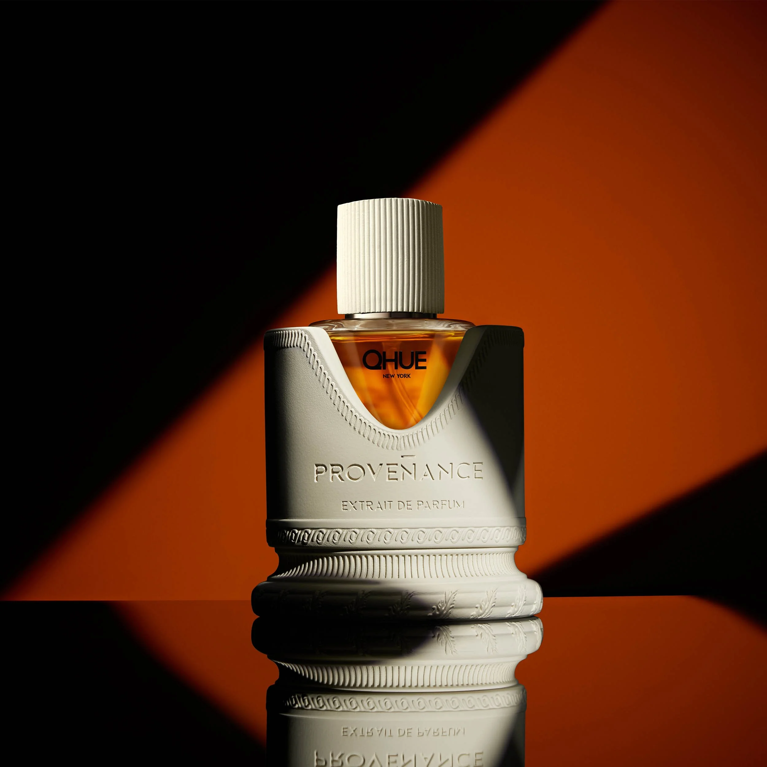 Qhue New York Provenance Extrait de Parfum luxury fragrance with dramatic orange and black lighting on a reflective surface.