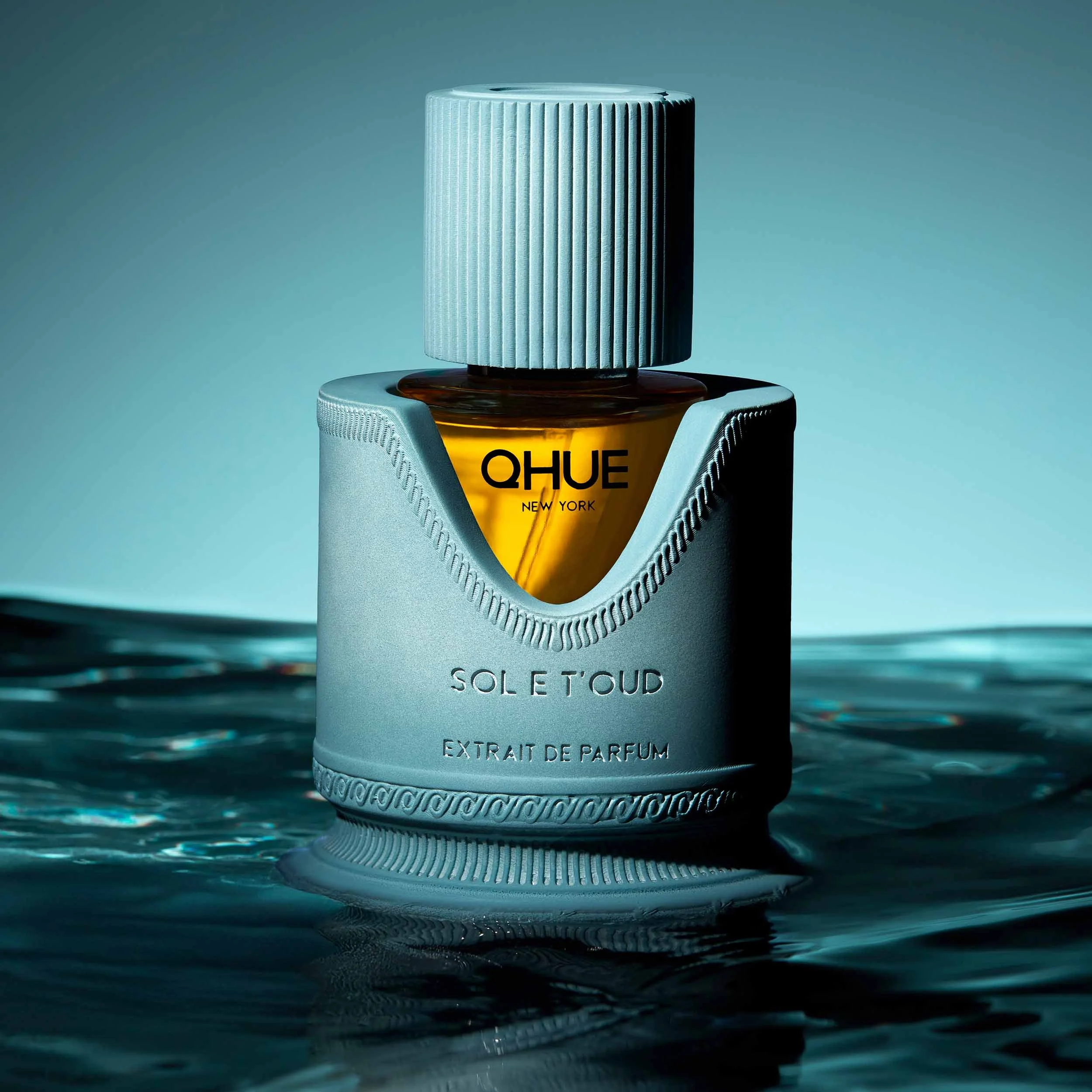 Qhue New York Sol e T'oud Extrait de Parfum luxury fragrance on reflective water with cool blue lighting.