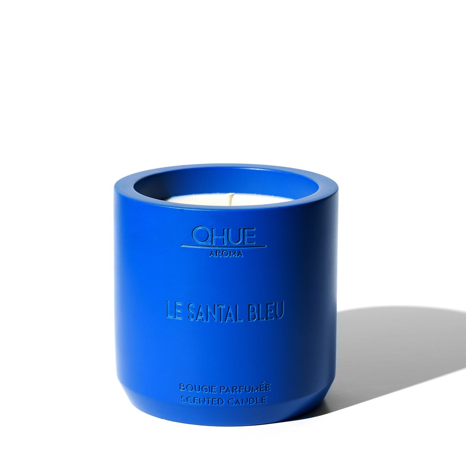 Le Santal Bleu candle featuring a sleek design with a deep blue hue, elegantly presented with a flickering flame, exuding the warm, exotic aroma of sandalwood and spices