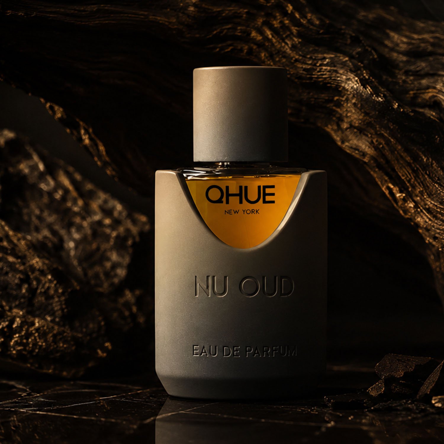 Qhue New York Nu Oud Eau de Parfum luxury fragrance bottle on black marble with dark wood in a moody campaign setting.