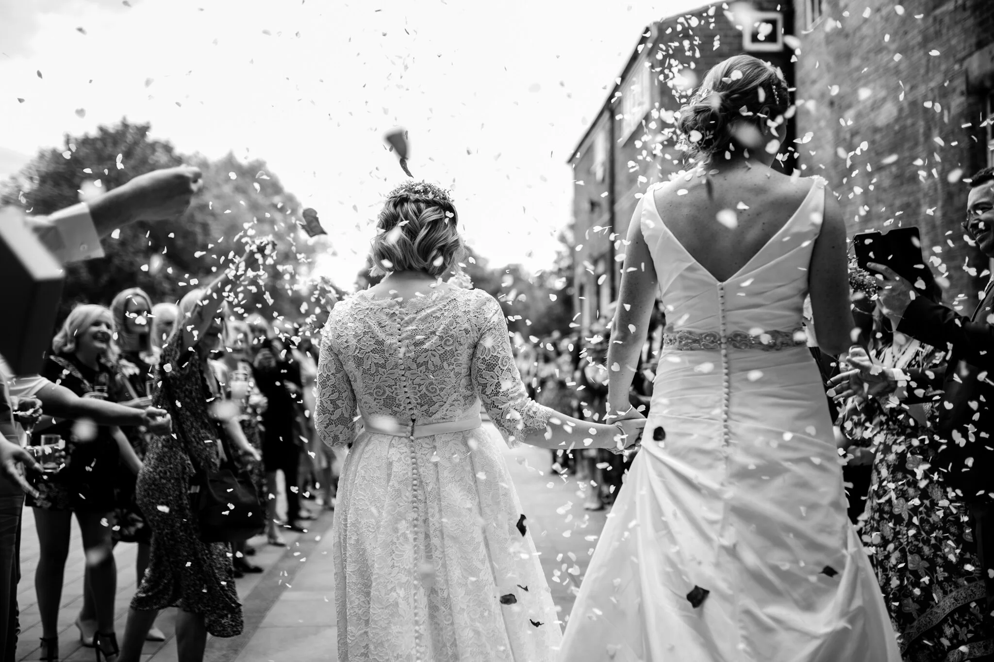 two brides walk away from the camera towards their wedding guests throwing confetti
