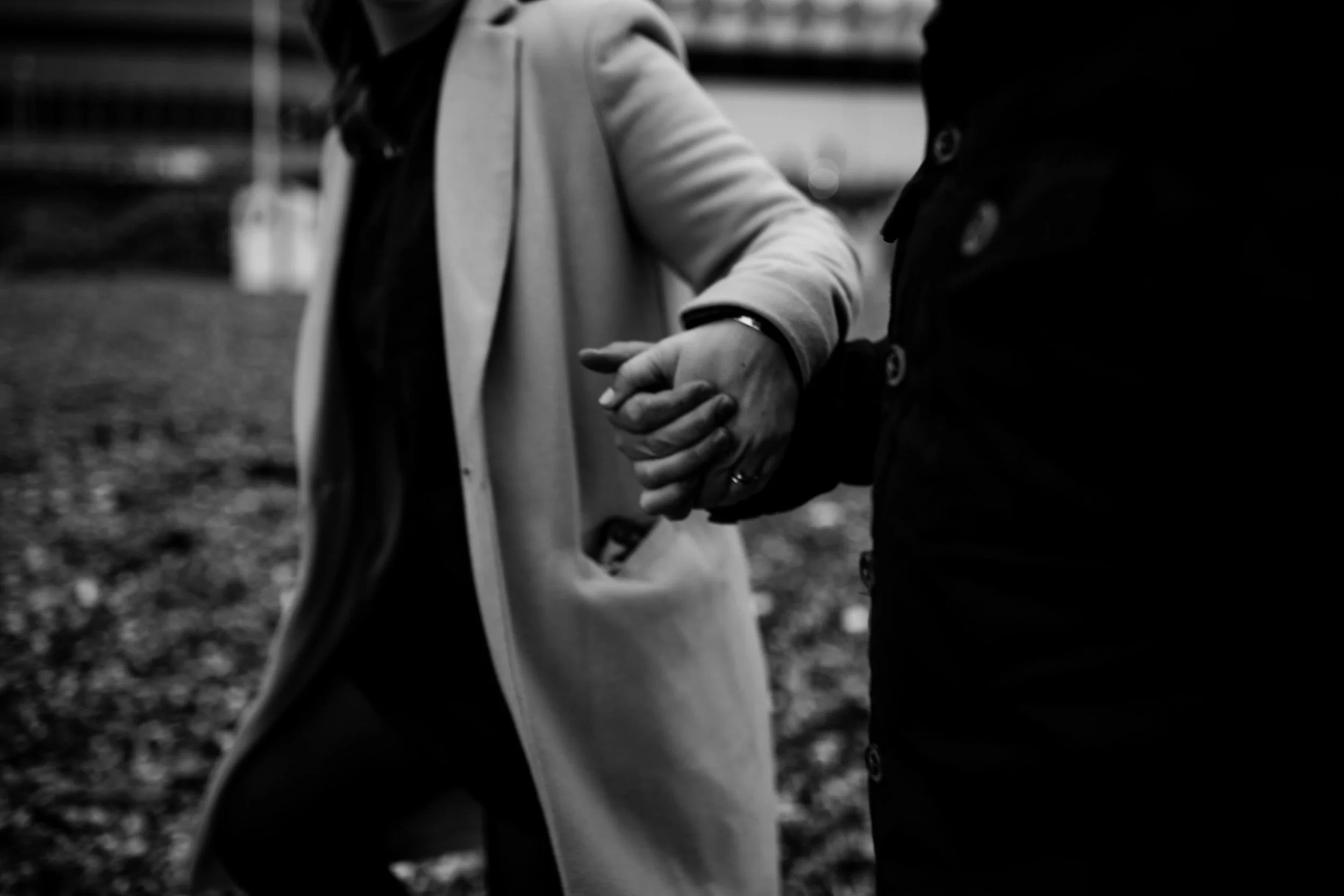 Black and white photo of two people holding hands, wearing coats, walking.