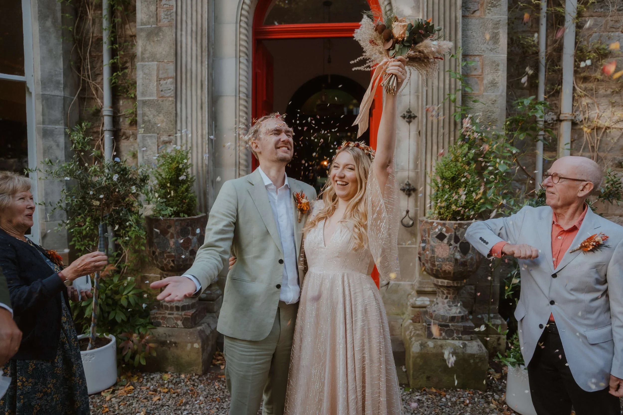 Bride and groom celebrating outside a vegan hotel with guests throwing confetti.