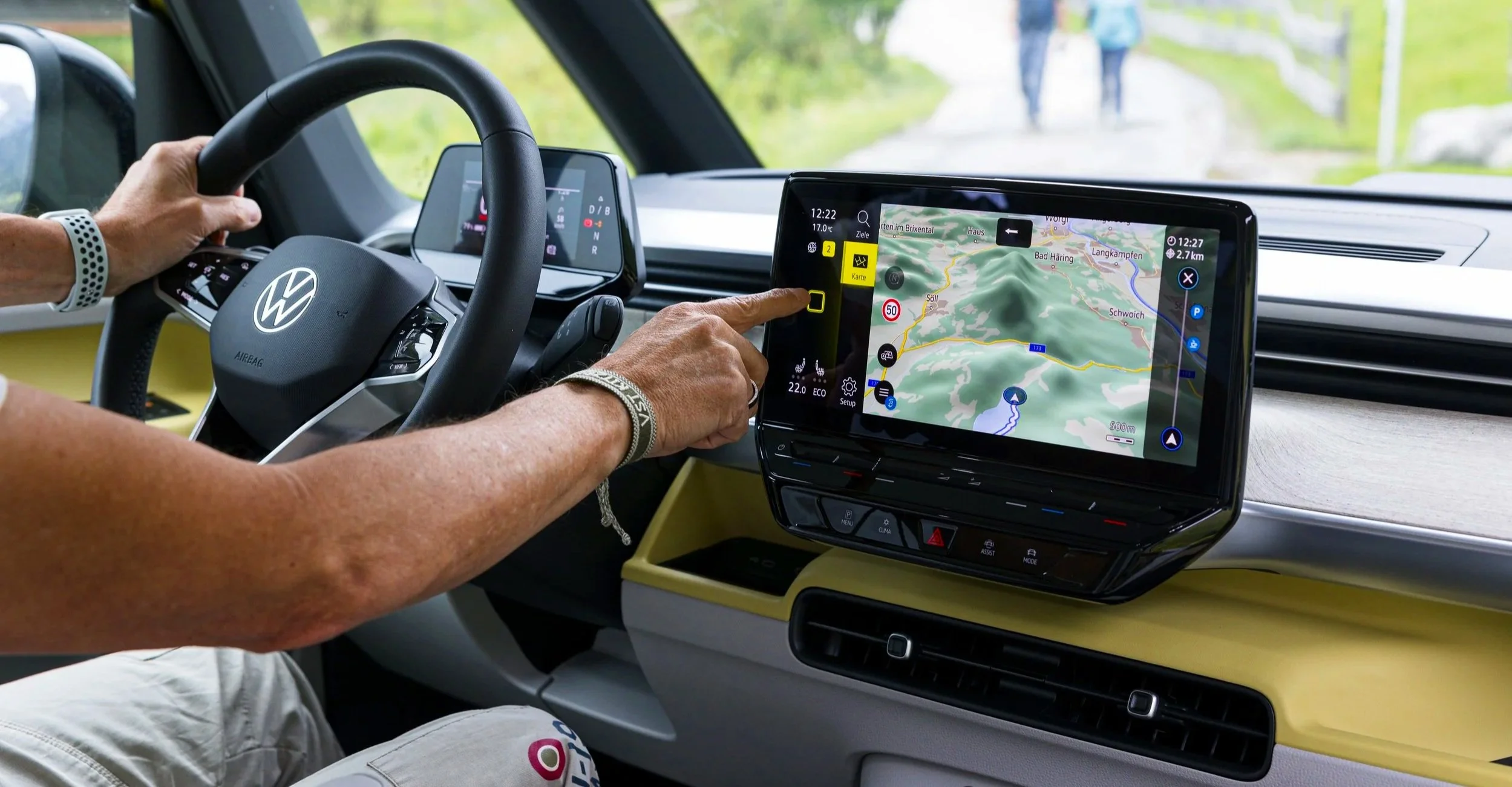 Fahrer bedient ein Navigationssystem in einem modernen Fahrzeug, mit einer Hand auf dem Lenkrad und der andere auf dem Touchscreen, während die Straßenkarte auf dem Display angezeigt wird.