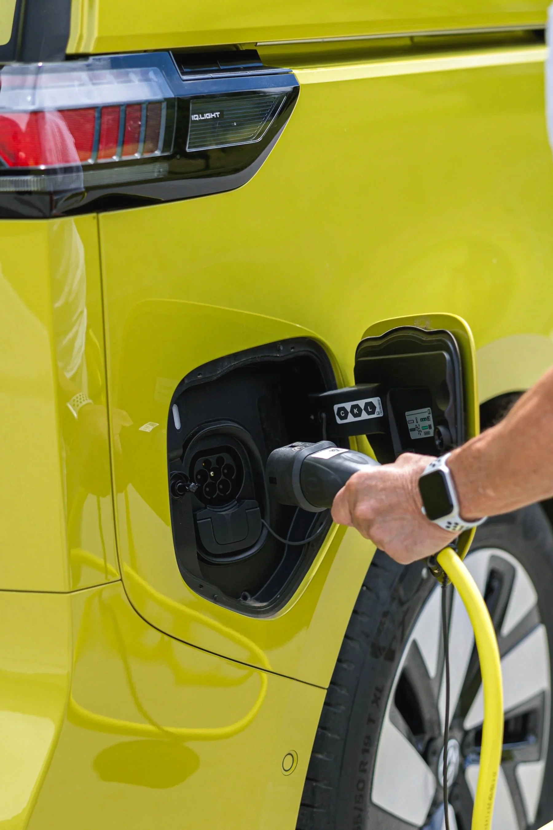 Ein gelber Elektroauto wird an einer Ladestation aufgeladen, die Person schließt das Ladekabel an das Auto an.