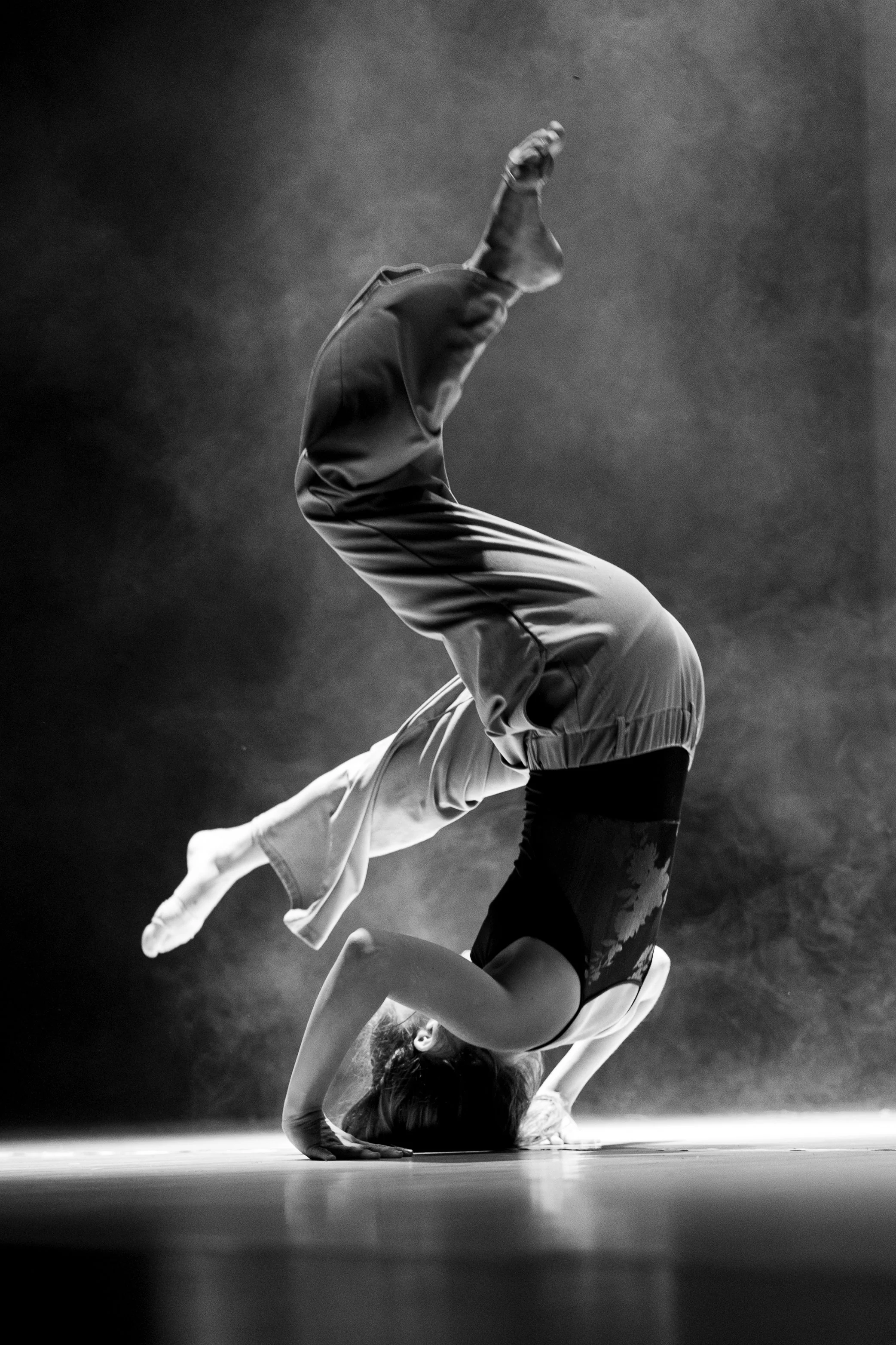 Eine Frau führt eine akrobatische Yoga-Posen auf der Bühne im schwarzen und weißen Schwarzweißbild aus.