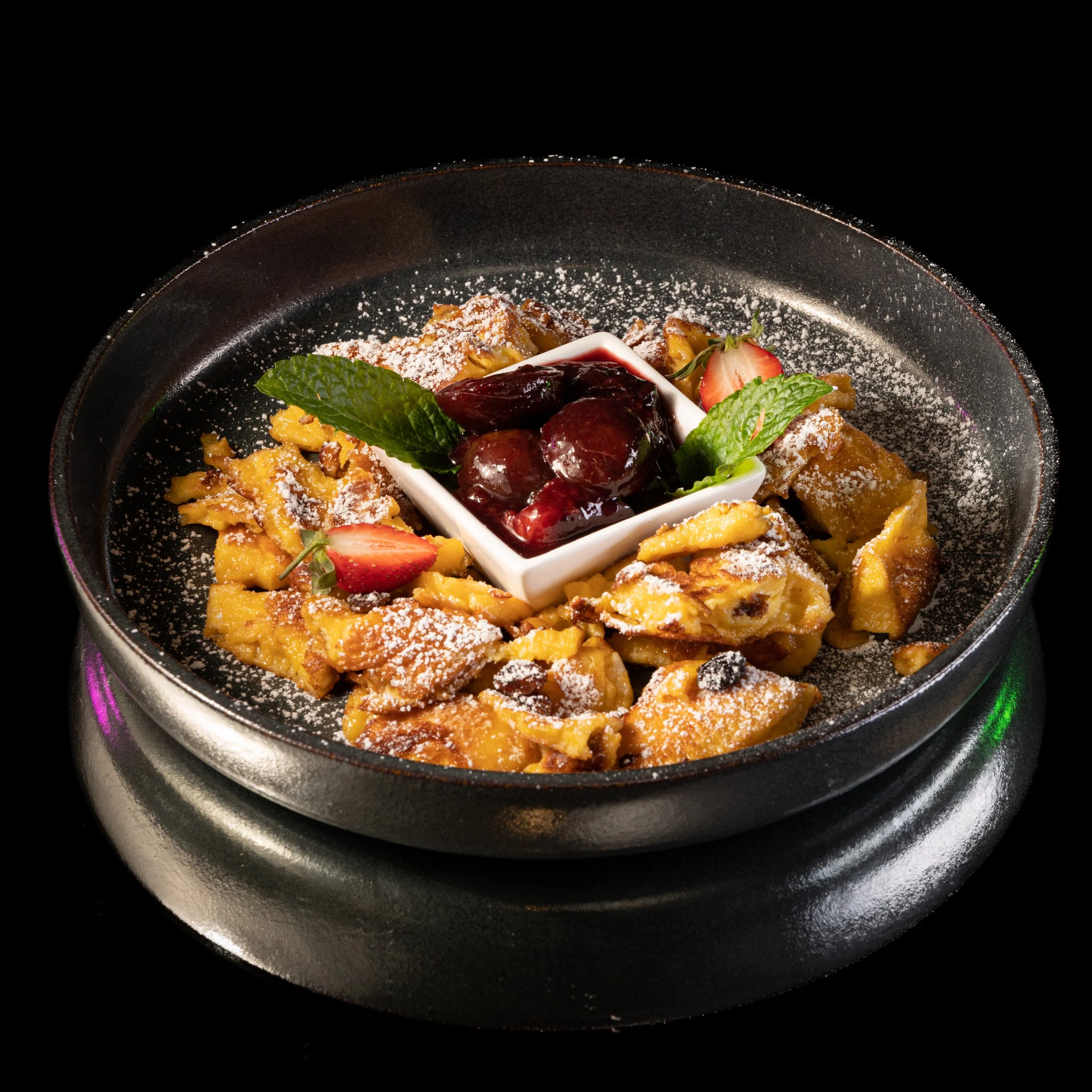 Obstauflauf mit Kirschen, Erdbeeren, Minzblättern, Puderzucker und Vanillesoße