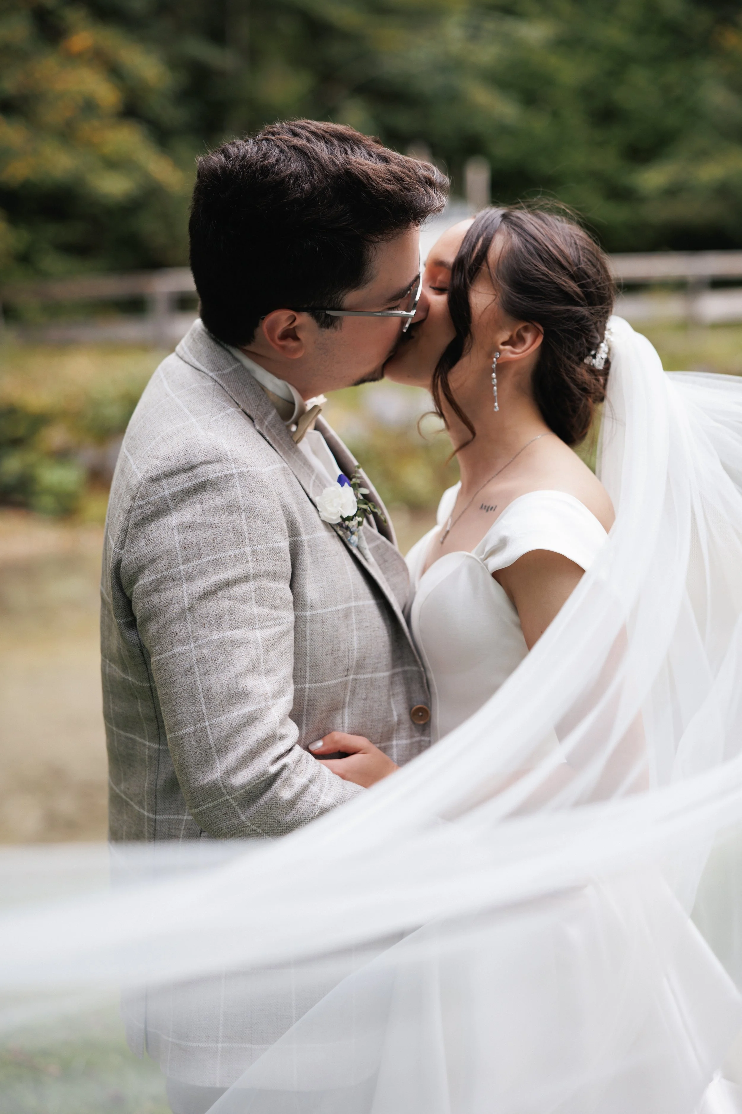 Ein Paar bei einer Hochzeitszeremonie küssen sich im Freien, mit Natur im Hintergrund.