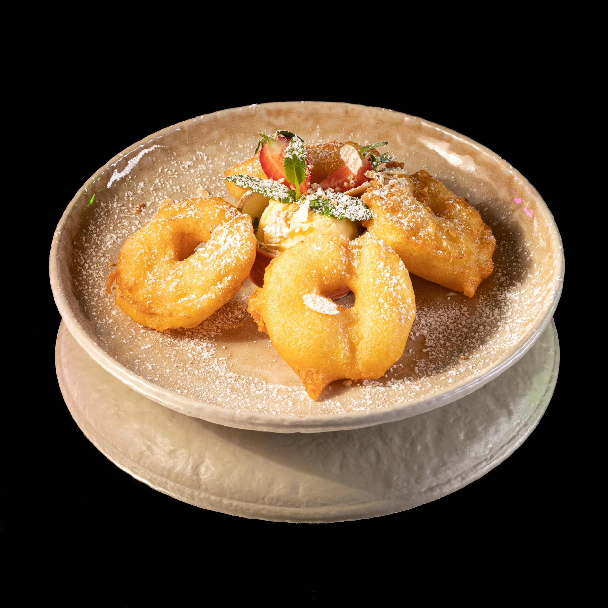 Frittierte Zwiebelringe und Hähnchenflügel auf einem Teller mit Marmelade, Erdbeere und Minzblättern, bestäubt mit Puderzucker, vor schwarzem Hintergrund.