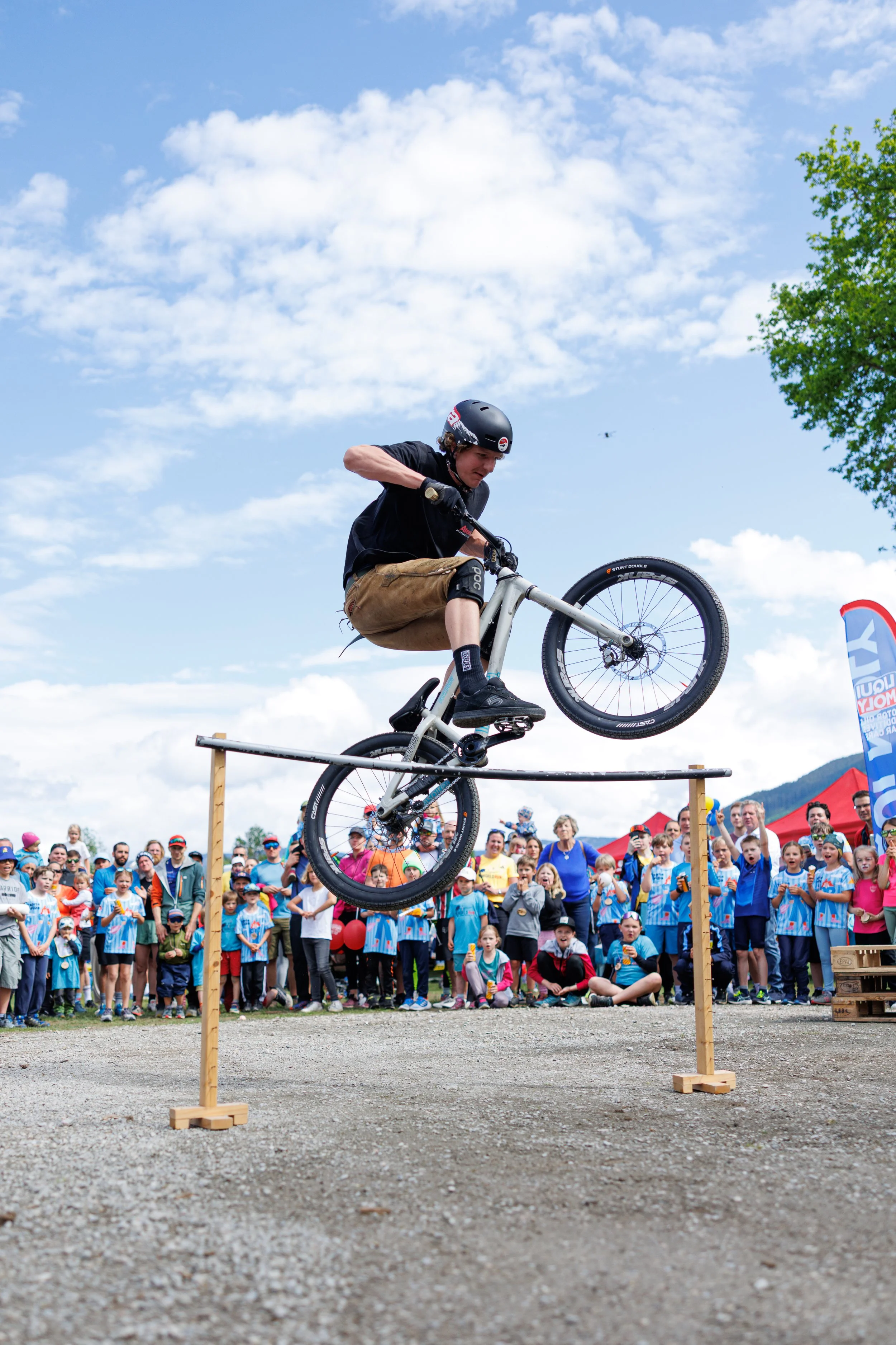 Ein Junge fährt auf einem Fahrrad über eine schmale Stange bei einem Fahrrad-Cross-Event, während eine große Menschenmenge im Hintergrund zuschaut.