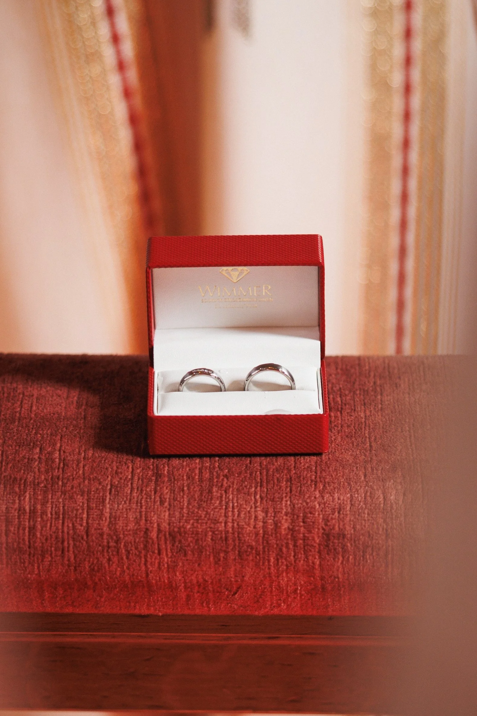 Eheringe in einer roten Geschenkschachtel auf einem roten Stoffhocker.