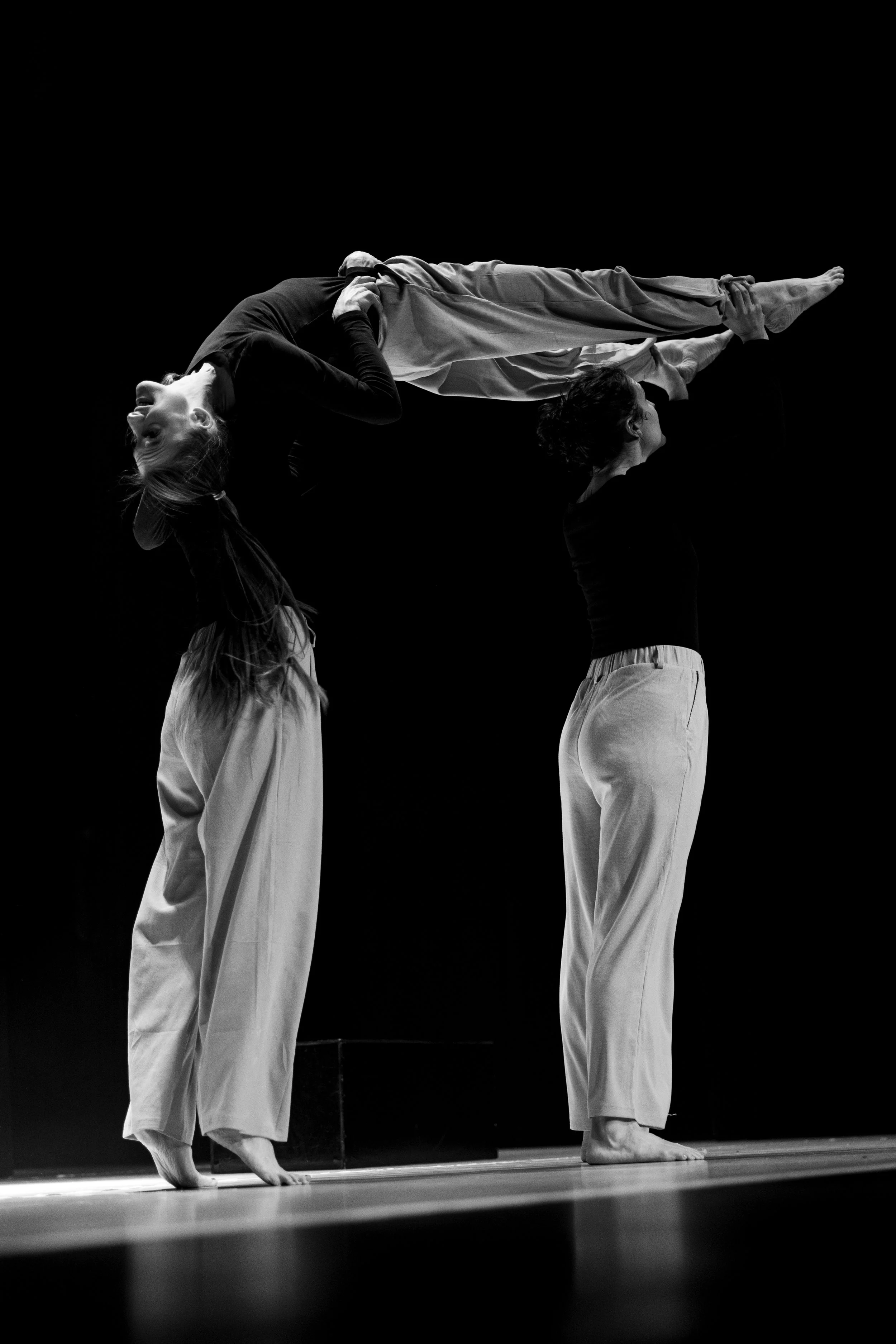 Zwei Tänzerinnen führen eine akrobatische Pose auf einer Bühne aus, eine hält die andere hoch in einer Bodenlage, schwarz-weiße Aufnahme.