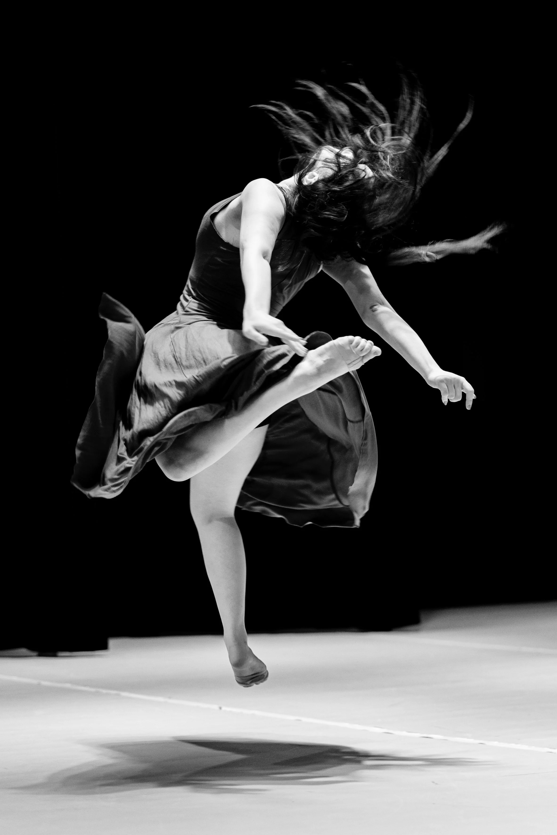 Schwarz-weiße Aufnahme einer tanzenden Frau in Bewegung, die in die Luft springt und einen dynamischen Tanz zeigt.