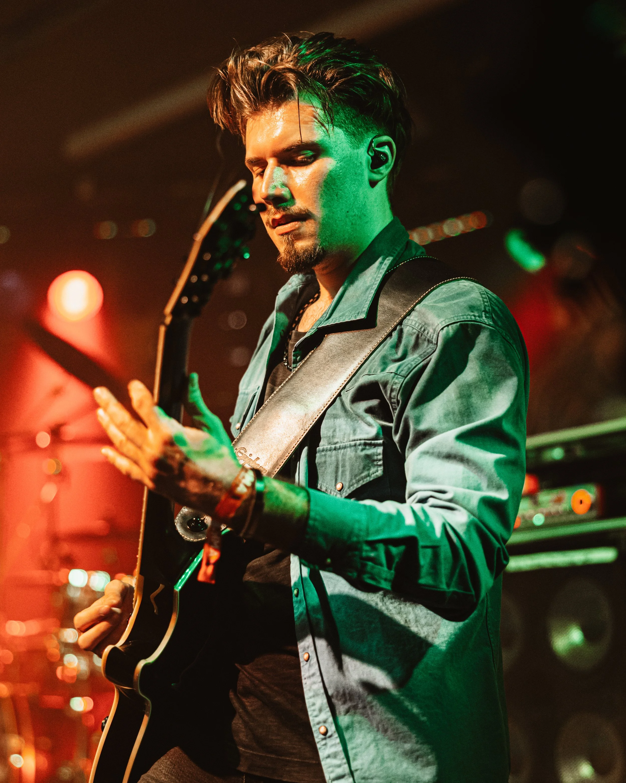 Ein junger Mann spielt Gitarre in einer Musikbar, beleuchtet mit bunten Lichtern.