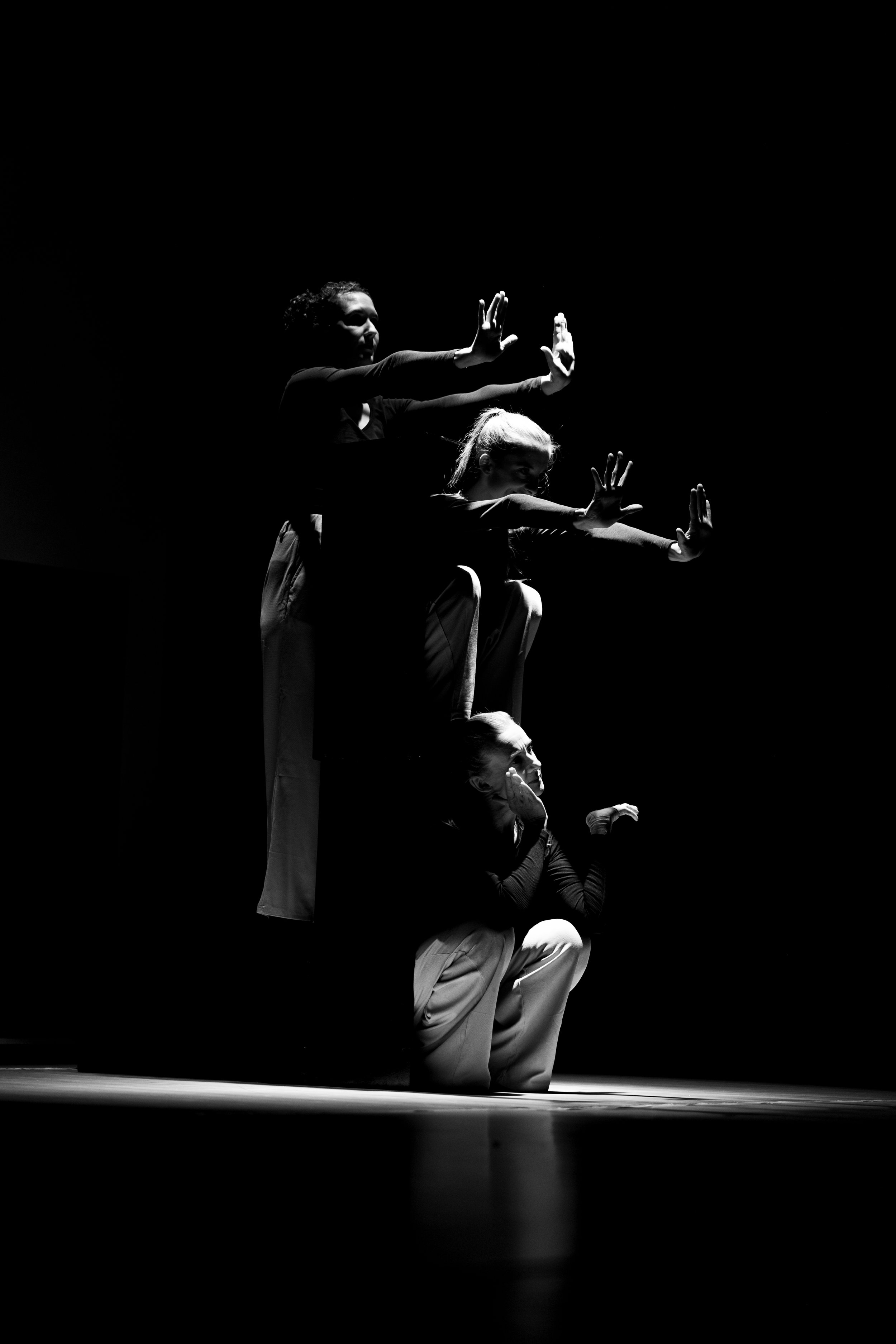 Drei Frauen auf dem Boden im Schatten mit erhobenen Armen in einer Choreografie.