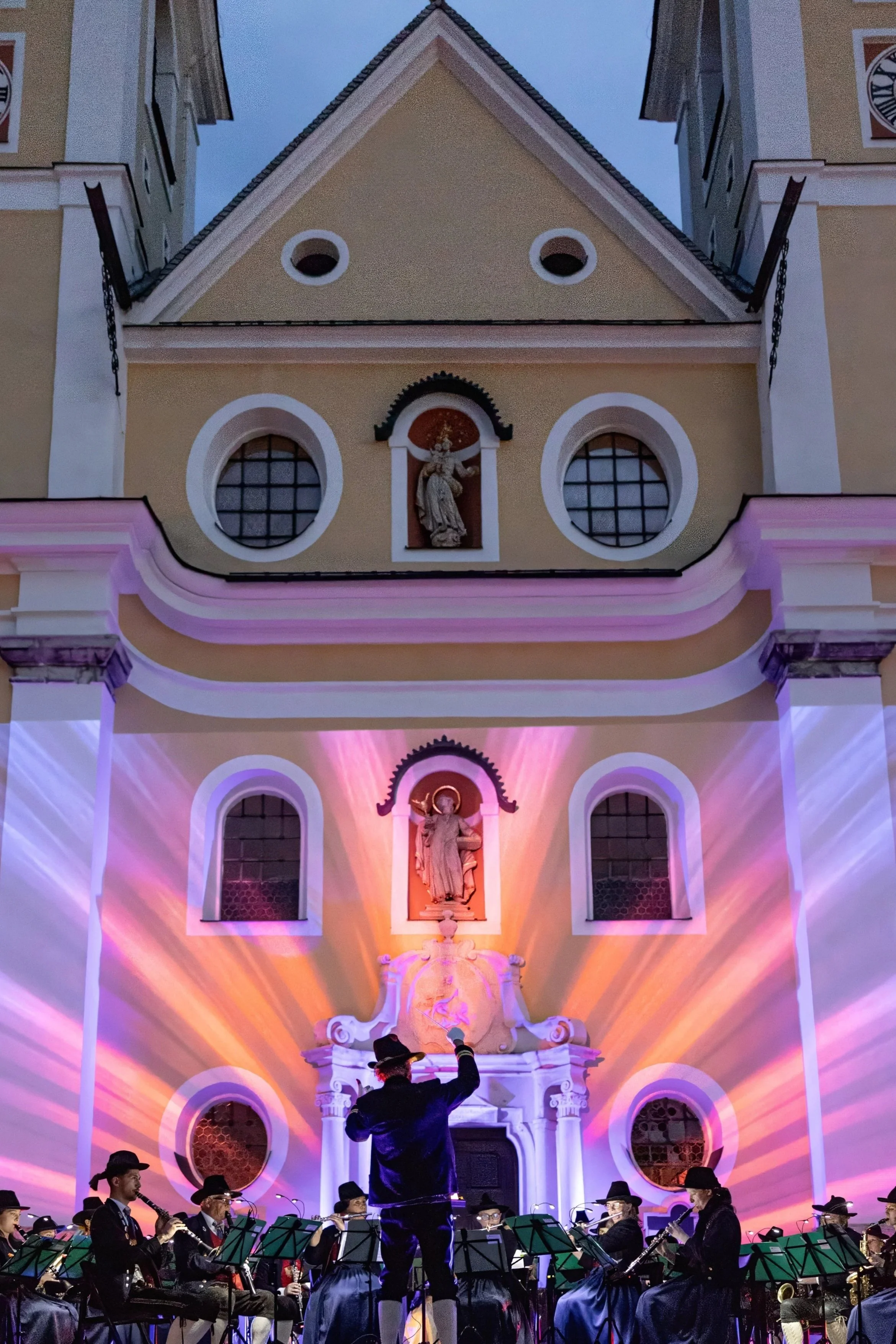 Orchester spielt vor einer barocken Kirche bei Nacht mit lila und orange Beleuchtung.