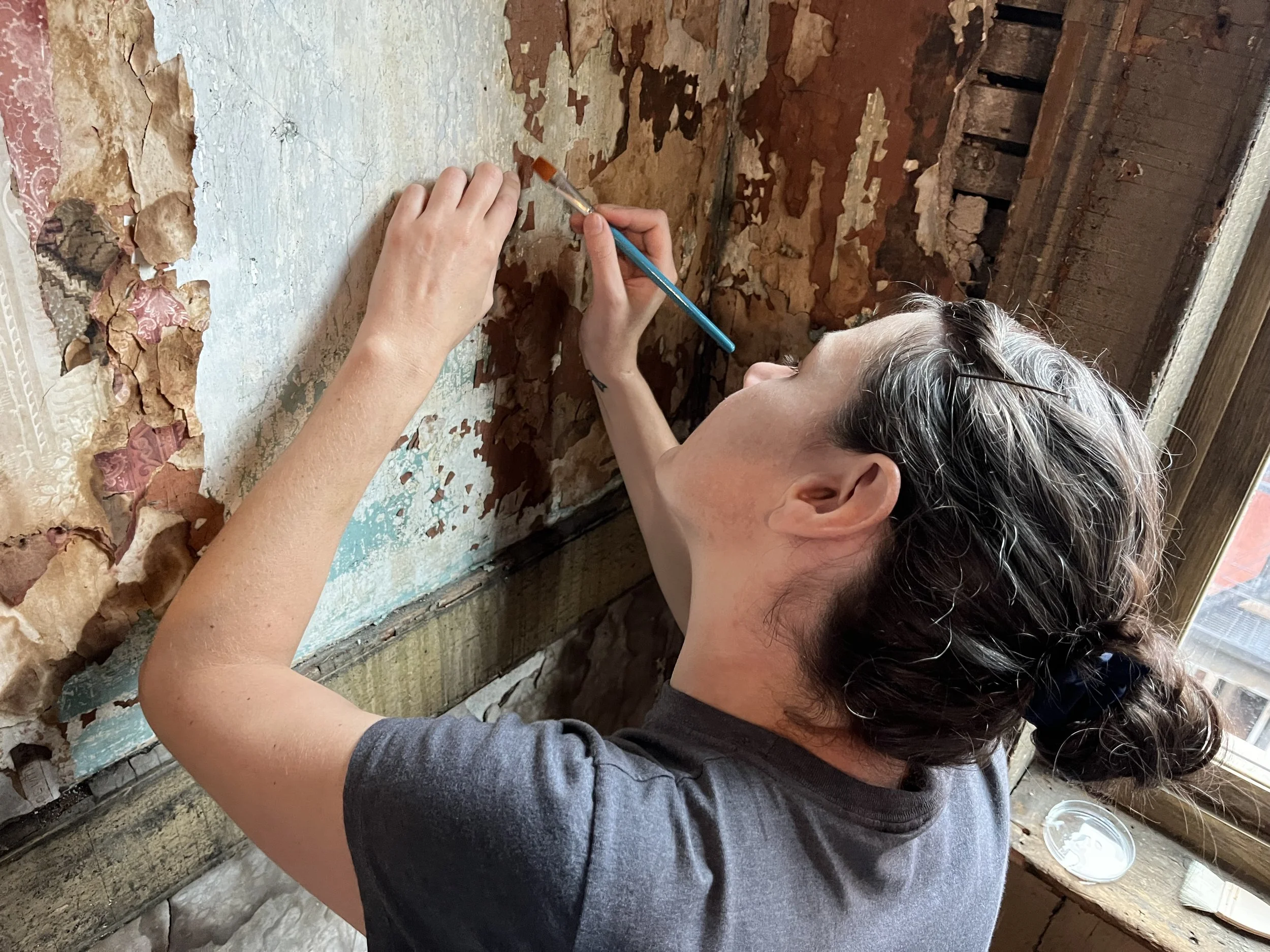 A conservator stabilizes flaking wall finishes.