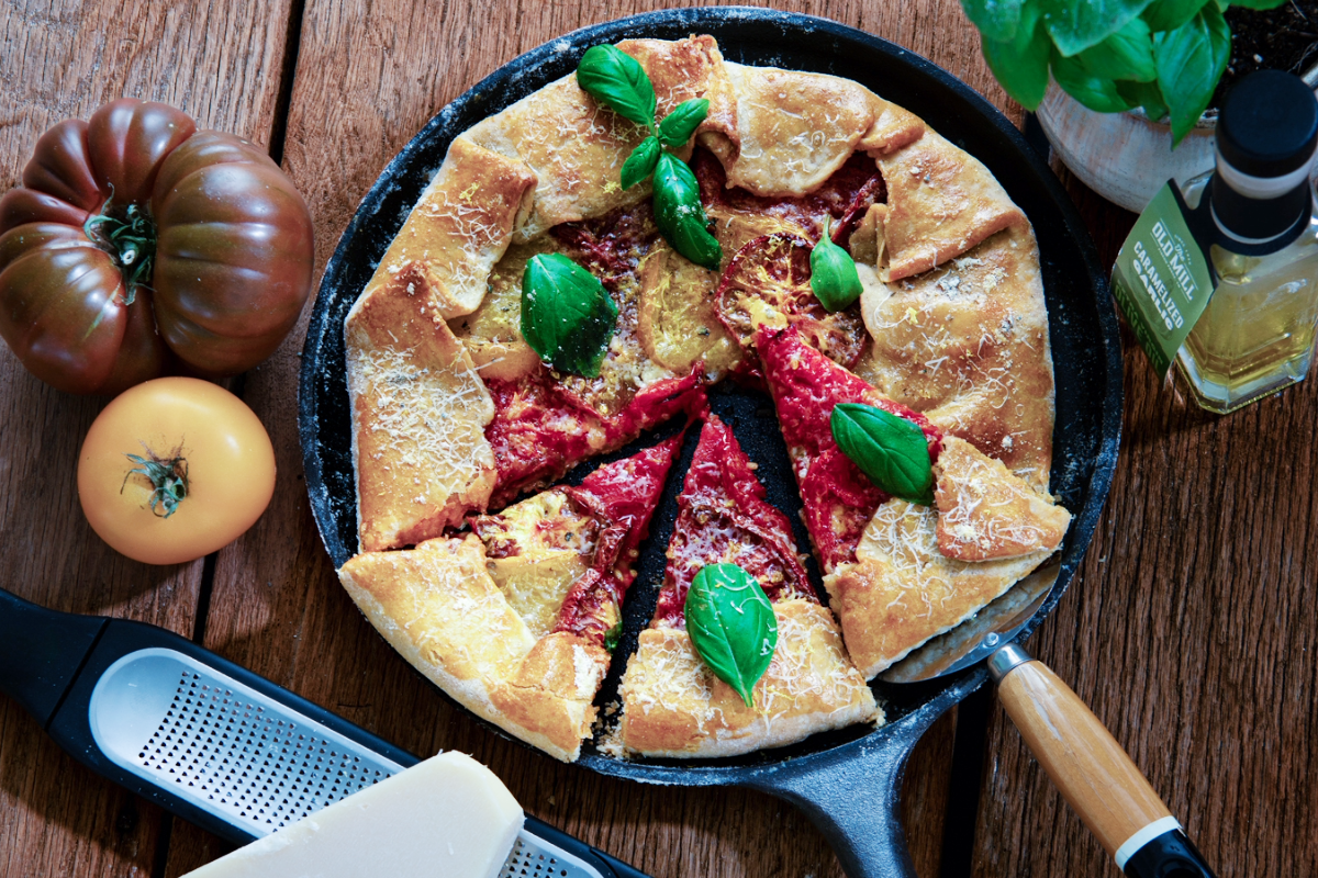 Tomato Galette in a cast iron skillet with fresh tomatoes on the side, with a block of cheese and a grater.