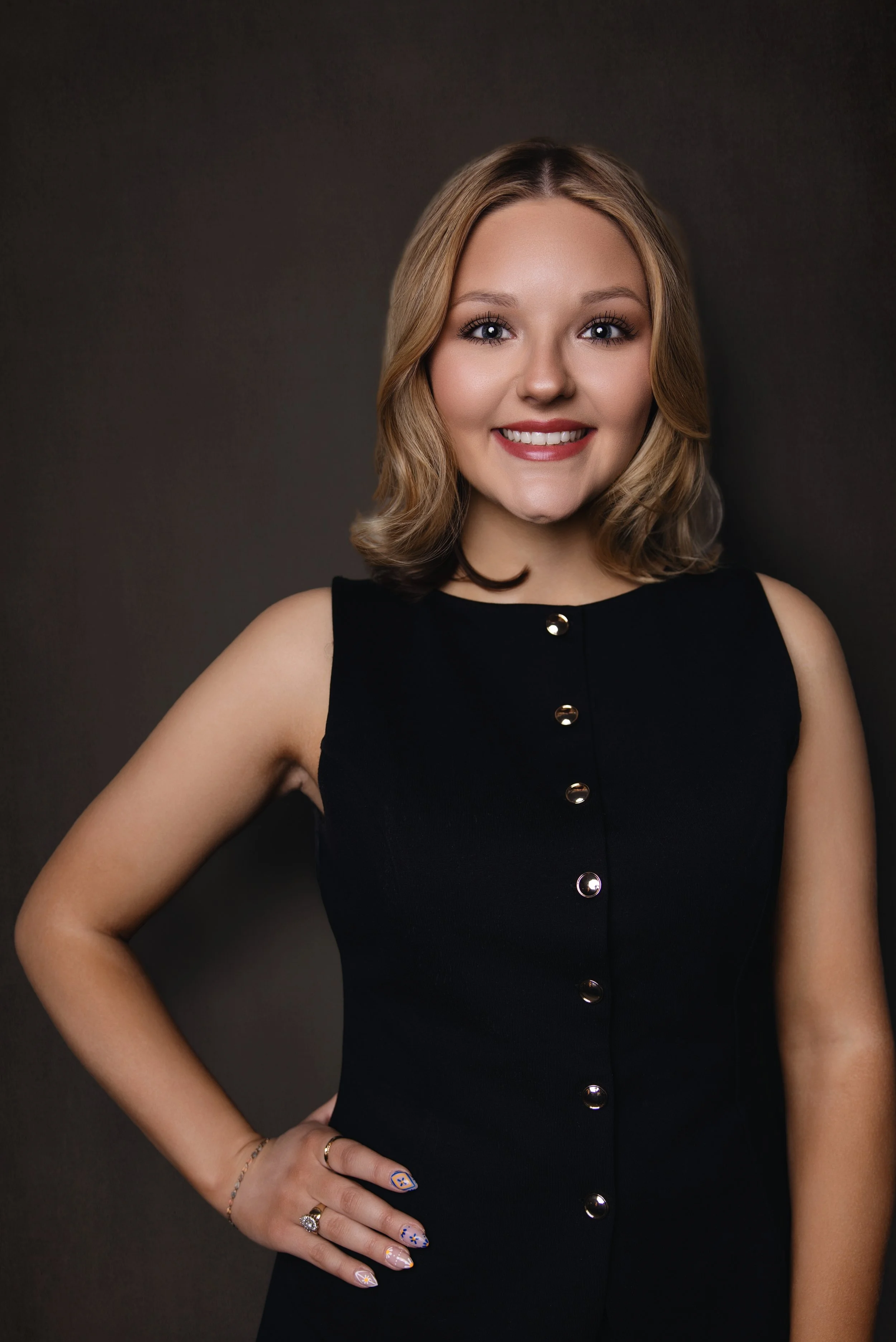 A woman with glasses, tattoos, and a black shirt sitting on a stool, smiling and looking at a silver MacBook. Kylee Ellis, Client Concierge at Monroe & Co Boudoir