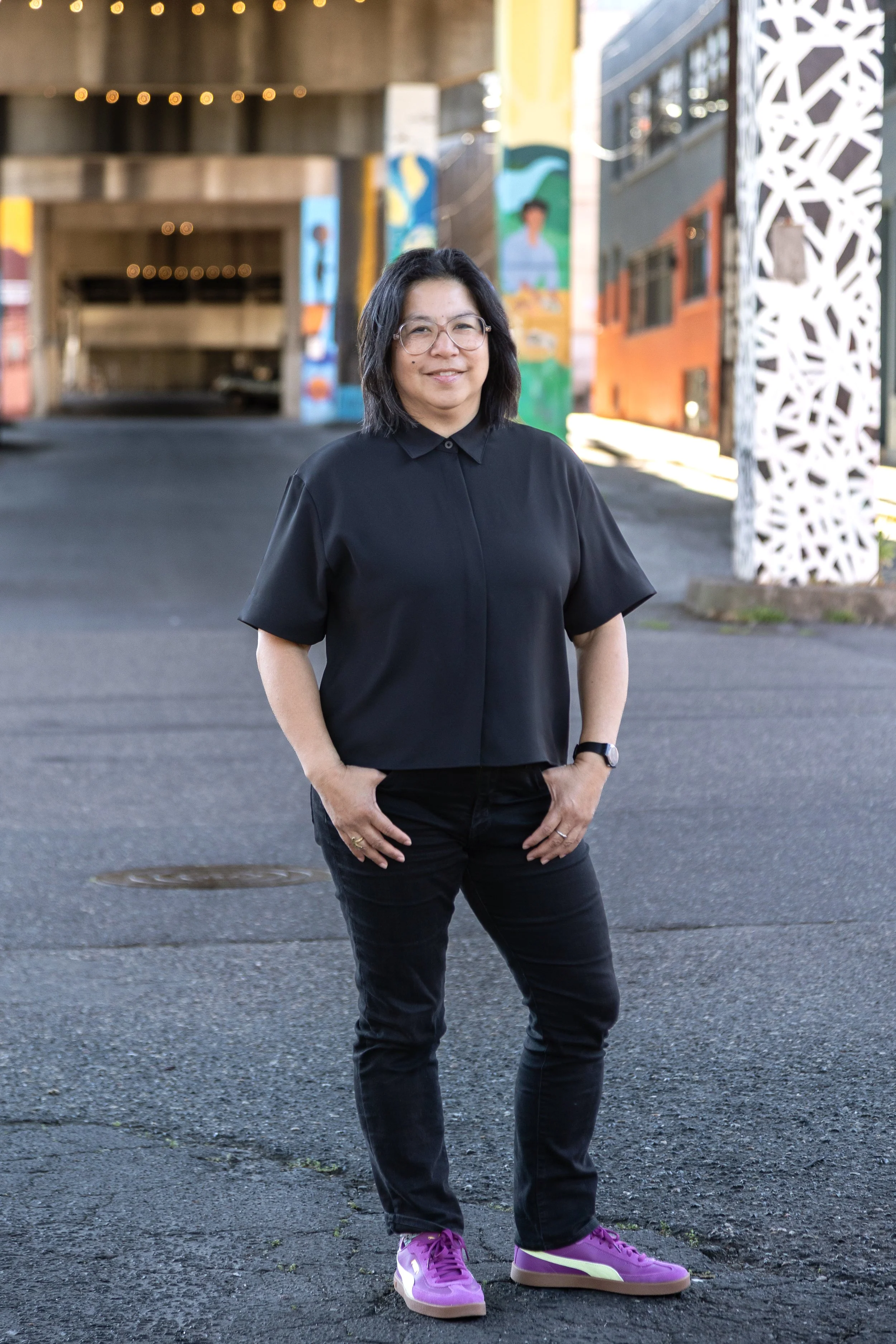 Photo of Filipino woman with black hair and glasses, dressed in black standing on the street