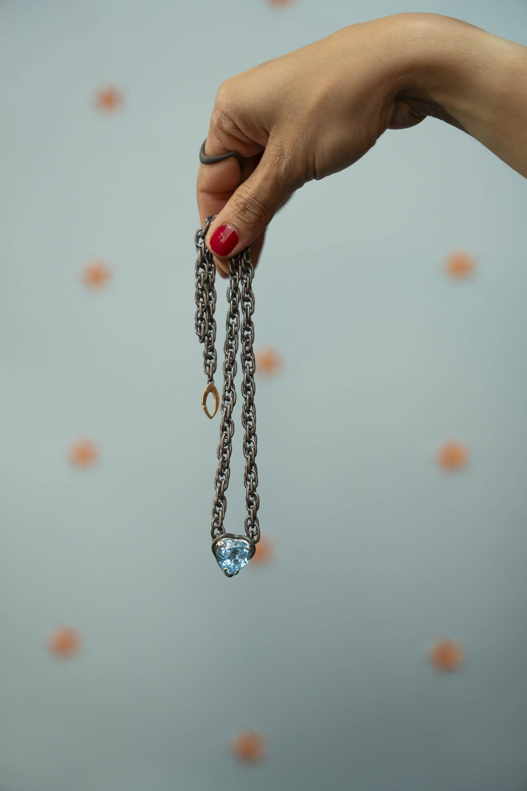 Hand holding a titanium chain, blue topaz heart-shaped pendant suspended