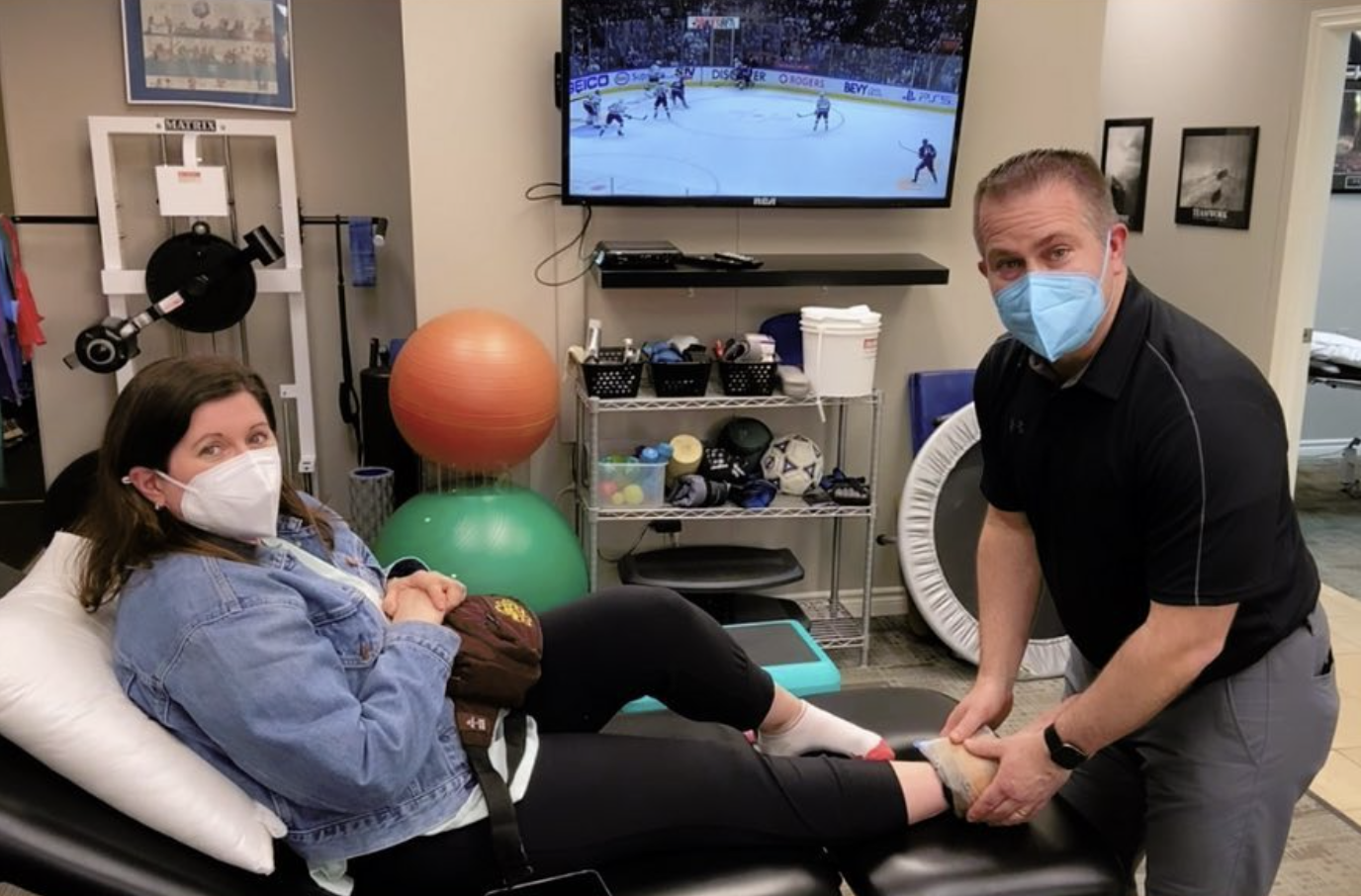Physiotherapist, Andrew Hoermann, is standing at the end of a treatment table holding an ice pack on the ankle of a client who is laying on the treatment table inside Mainway Physiotherapy.