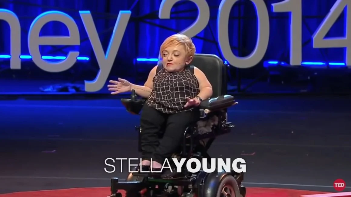 The picture is of Stella Young sitting in her power-chair on the TED Talk stage. Her name runs along the bottom of the image.