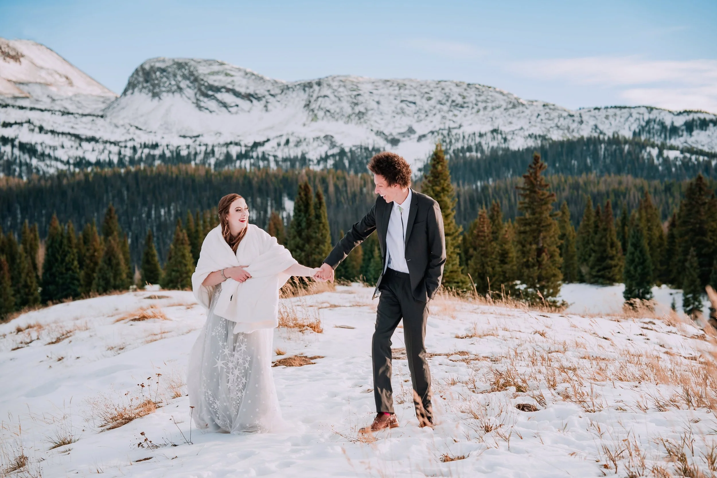 Bride and groom holding hands walking through snowy Colorado mountains