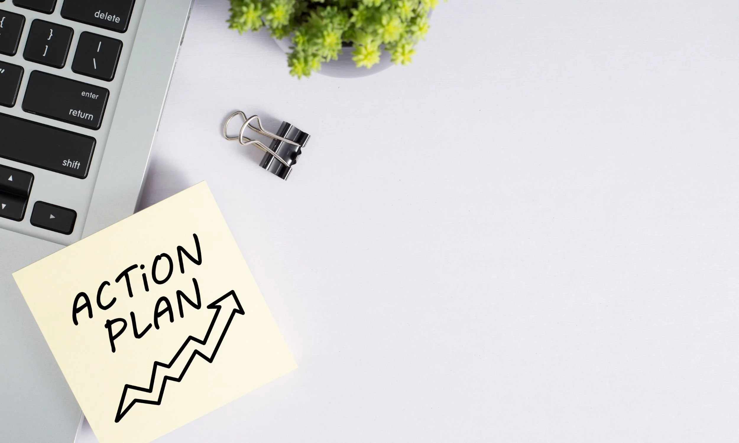 Sticky note with the words “ACTION PLAN” written on it and stuck on the side of a laptop.