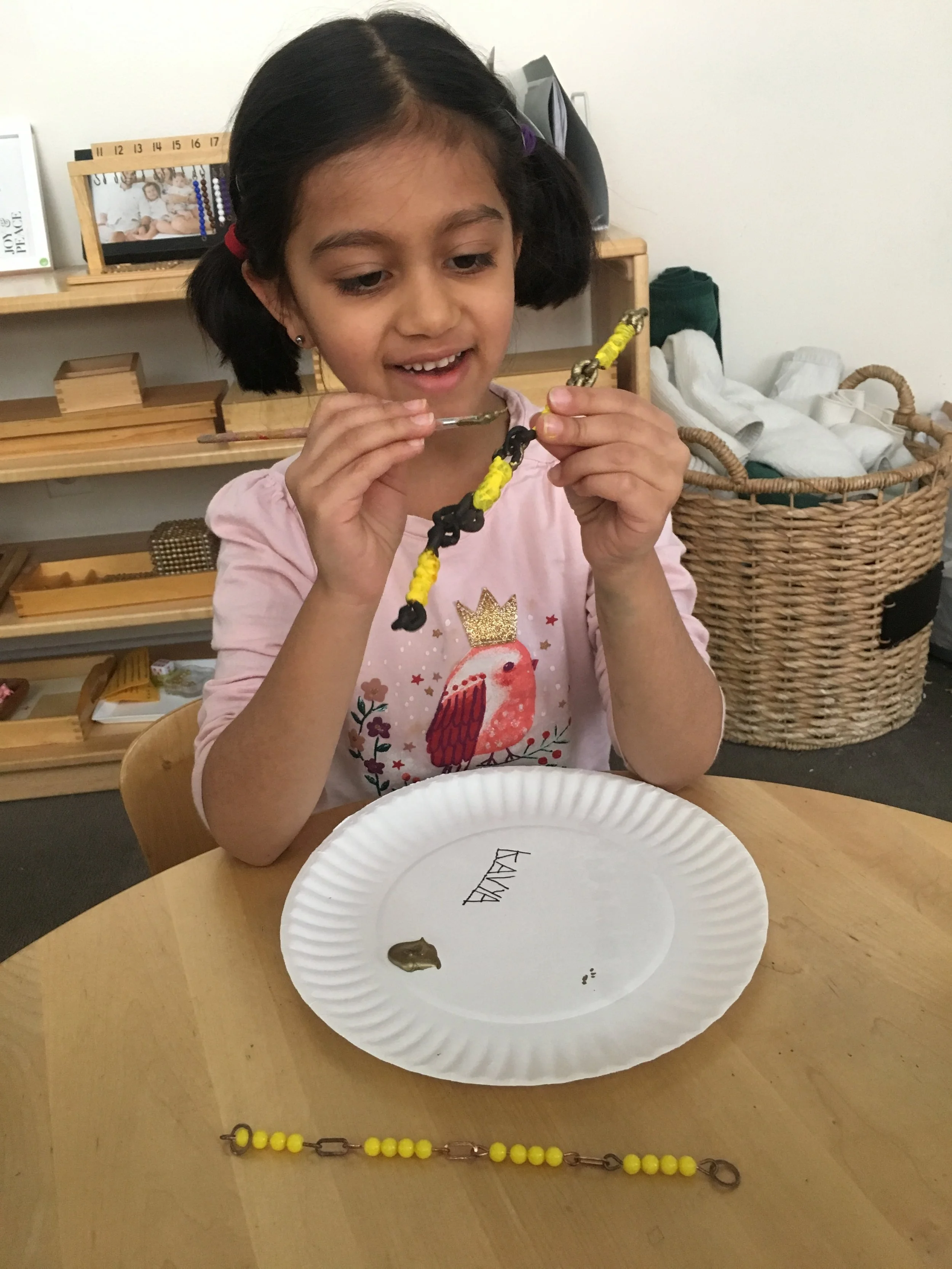 A child puts the finishing touches on a Short Chain she recreated in honor of Montessori week!
