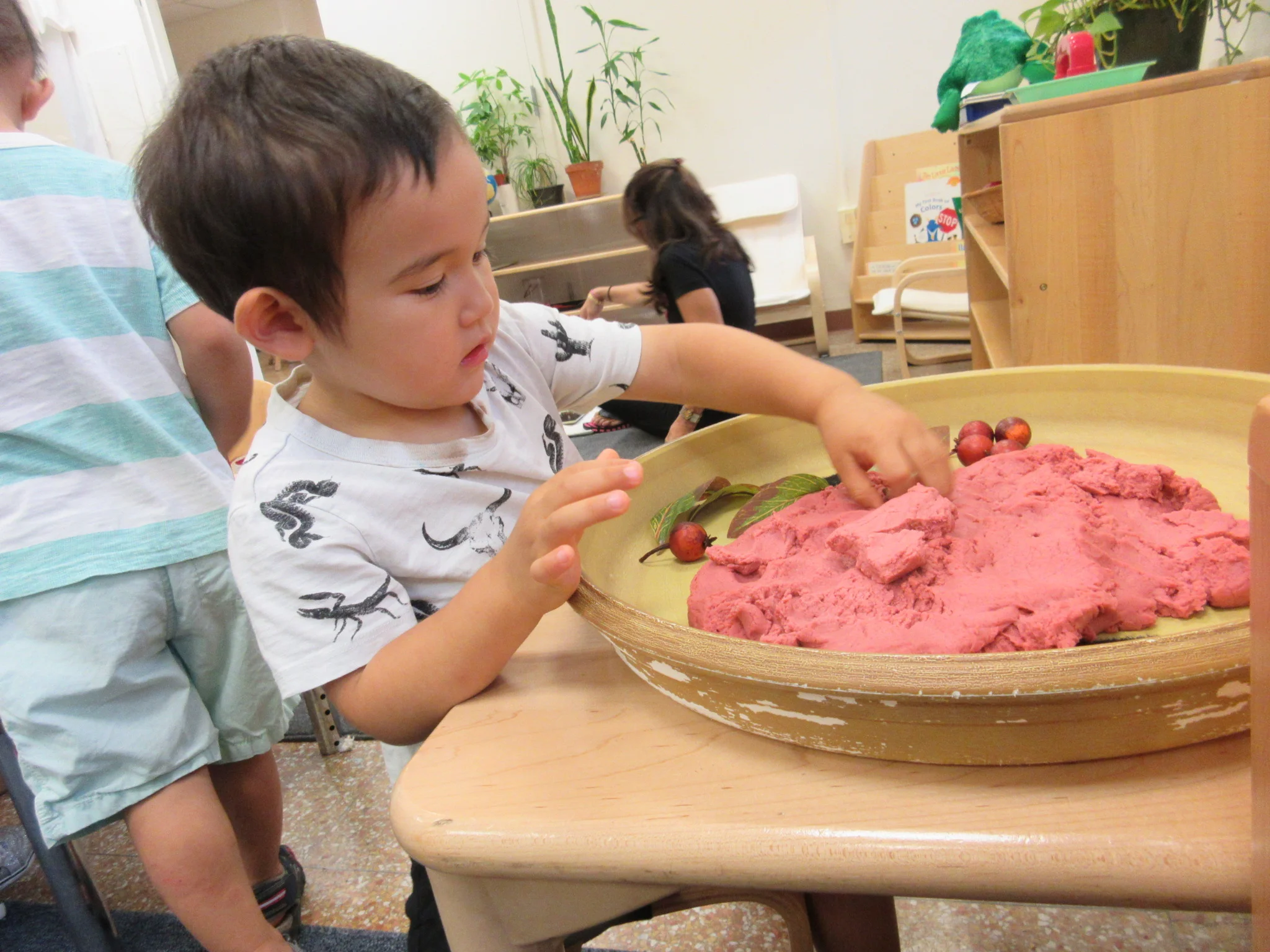 Working at the sensory table to find apples and leaves buried in the play doh 