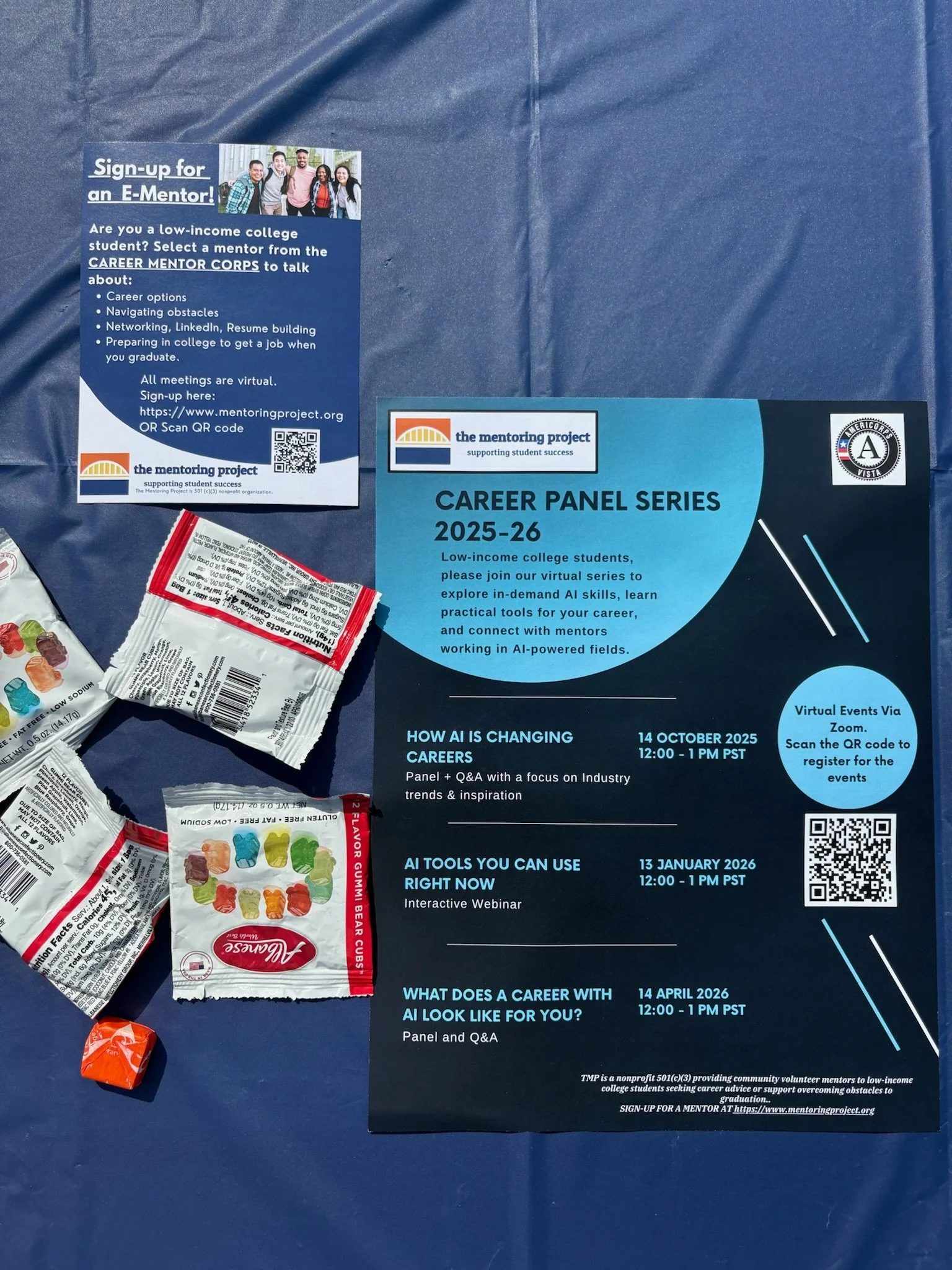 Flyers for the Career Panel Series 2025-26 and sign-up information for an E-Mentor program, along with scattered snack wrappers on a blue surface.