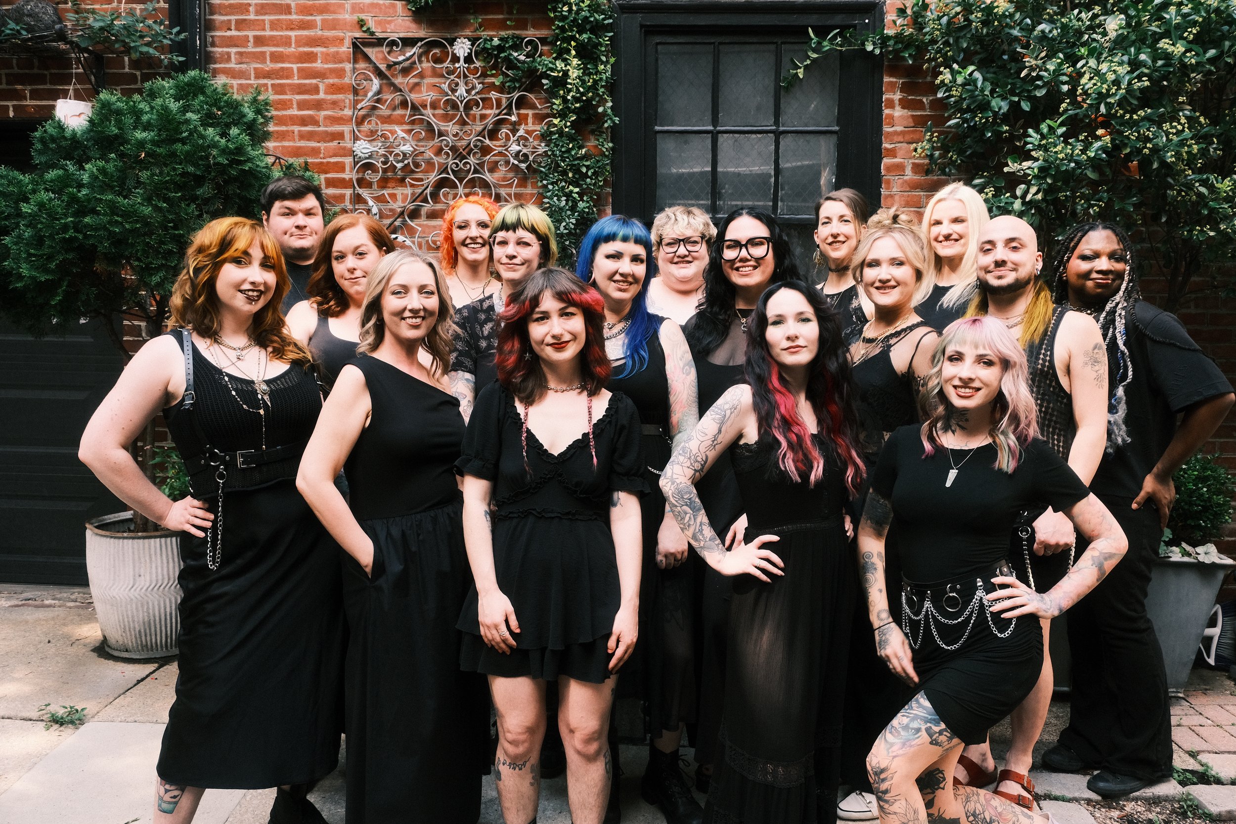 stylists group photo. in front of a red brick wall, with plants. stylists are wearing black and look very happy