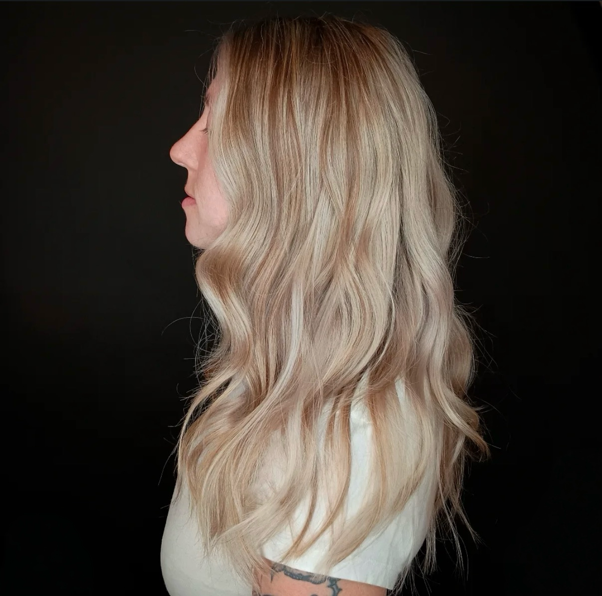 Side view of a woman with long, wavy blonde hair against a black background.