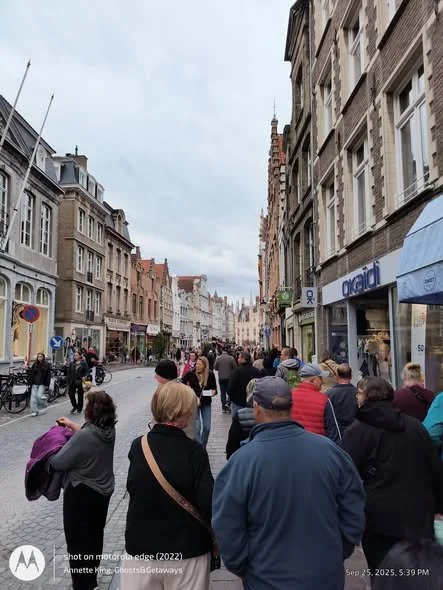 Busy city street with people walking and shopping outside stores, including an 'Orsay' clothing store, under cloudy skies.