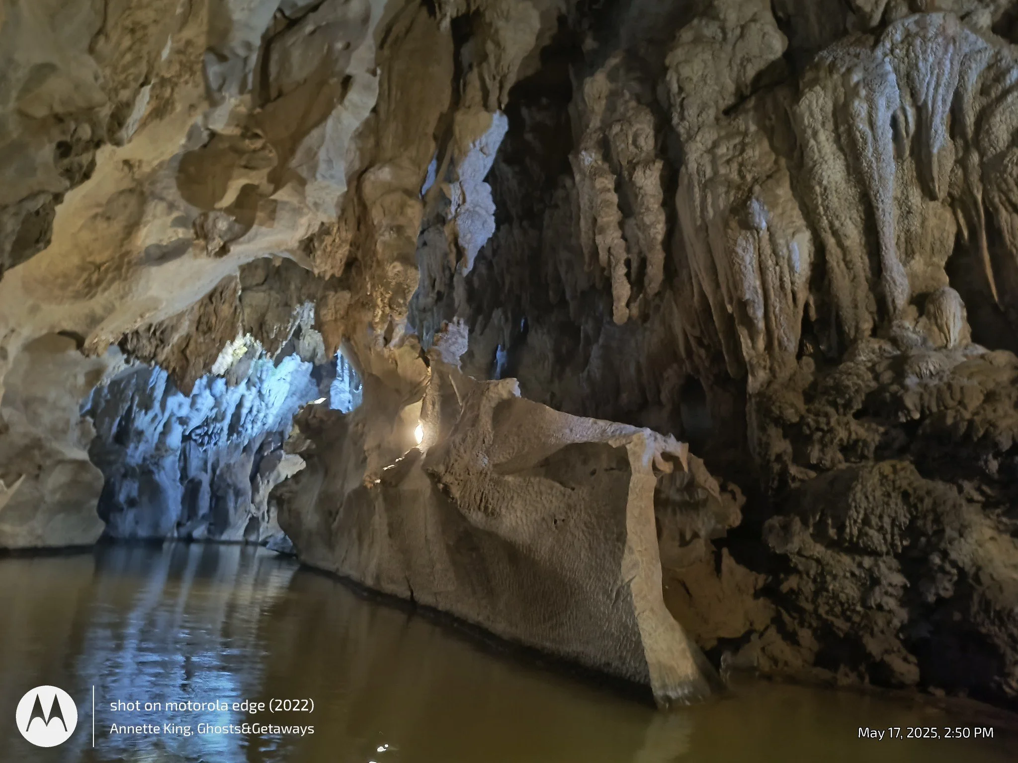 Inside a dark cave with stalactites hanging from the ceiling and a pool of water reflecting the rocky formations.