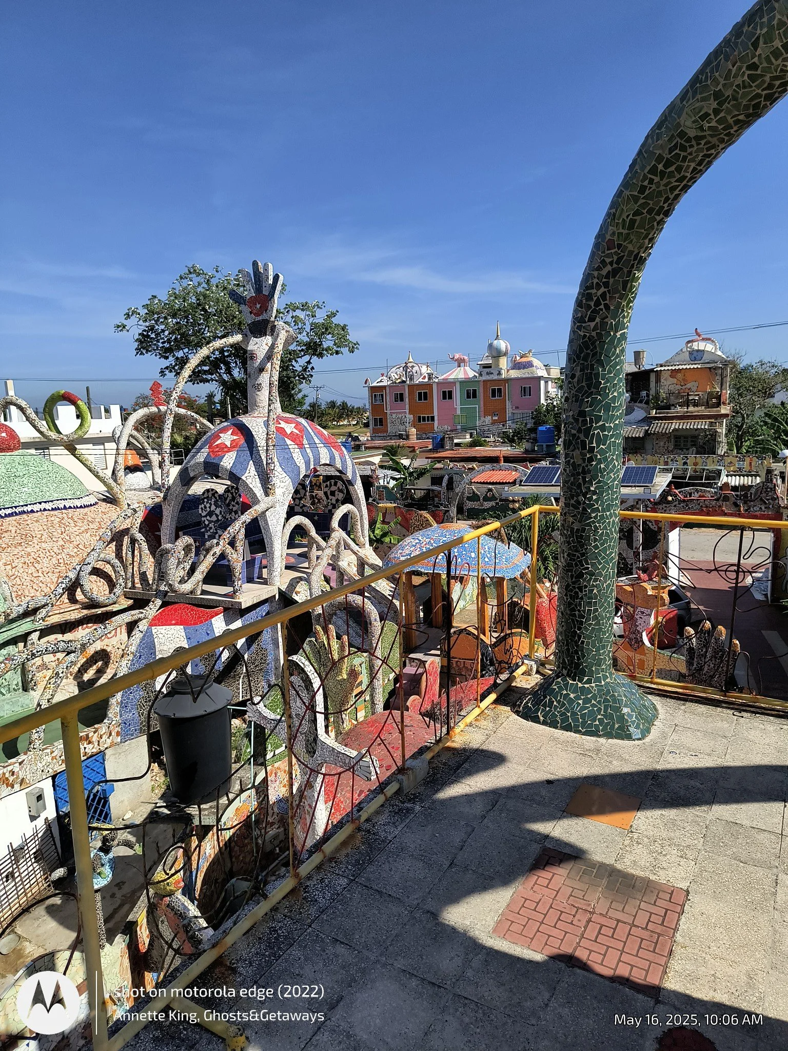 Colorful mosaic sculptures and a building with geometric shapes and pastel colors on a sunny day.