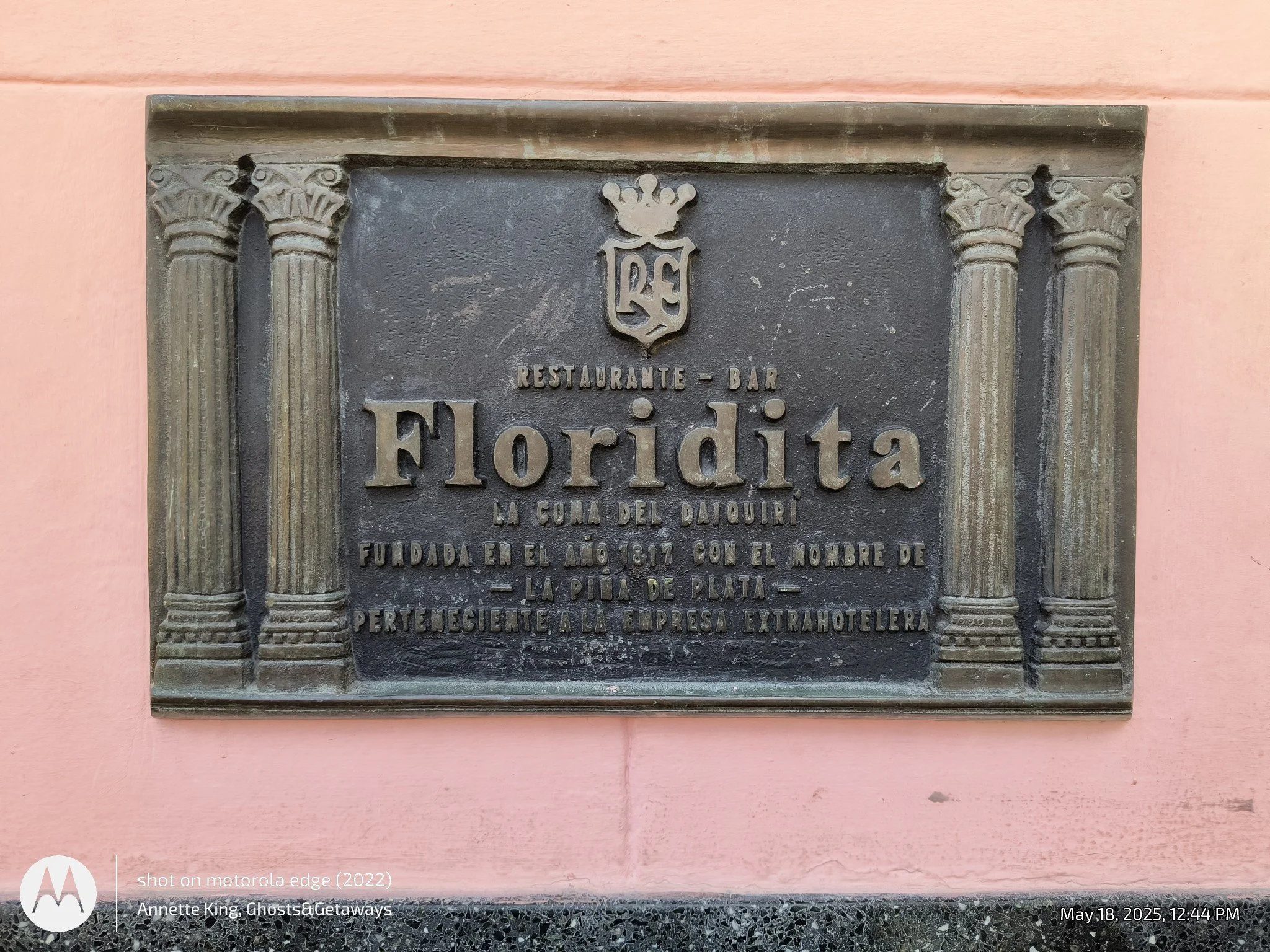 A historical plaque mounted on a pink wall. The plaque has decorative columns on each side and an emblem at the top with the letters 'RE'. The text on the plaque is in Spanish. It commemorates the founding of a restaurant and bar named Florida in 181