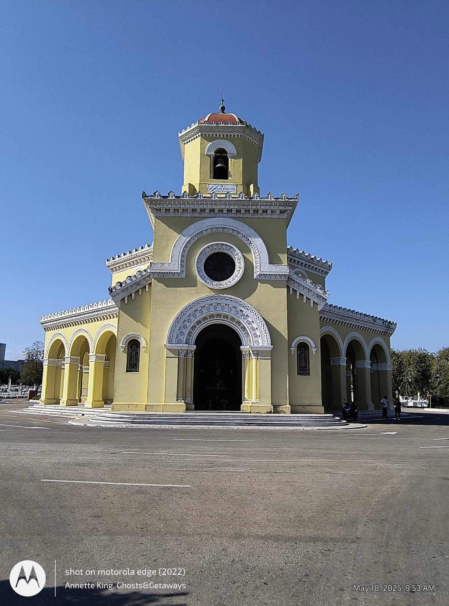 Colorful church building with a tall clock tower, arched entrances, and decorative trim, set against a clear blue sky.