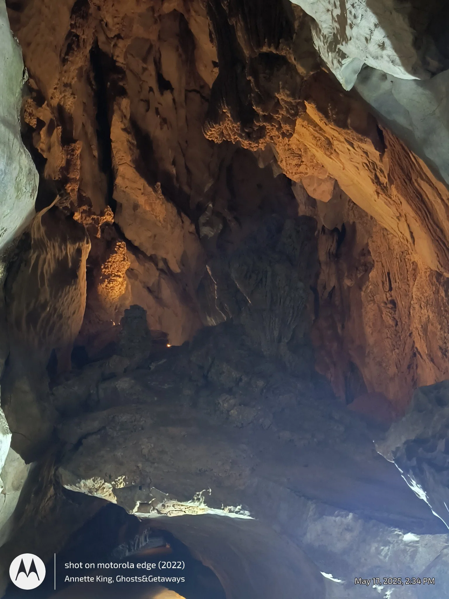 Interior of a large, dark cave with rugged rock formations illuminated by some light source.