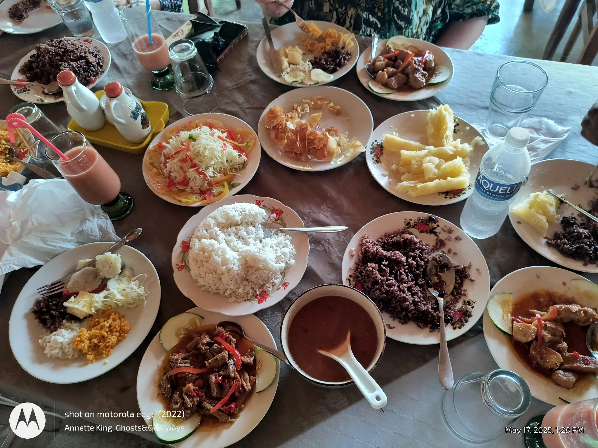 A large table filled with assorted dishes including rice, salad, meats, and vegetables, along with glasses, bottles of water, and beverages, set for a meal.