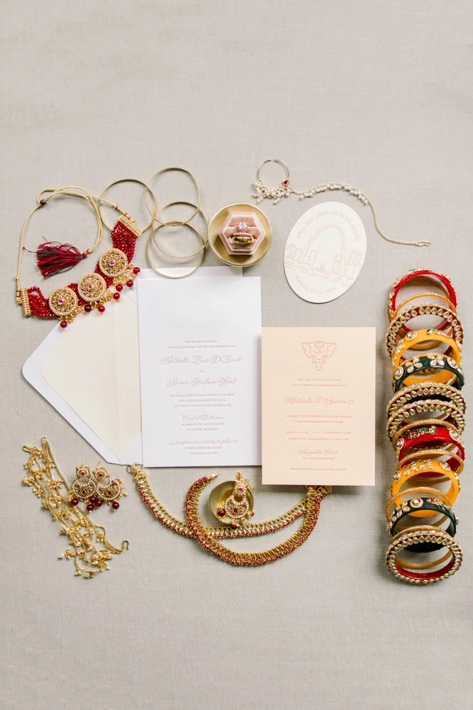 Indian wedding jewelry and invitations flat lay with bangles, necklaces, earrings, and letterpress wedding suite on a fabric background.