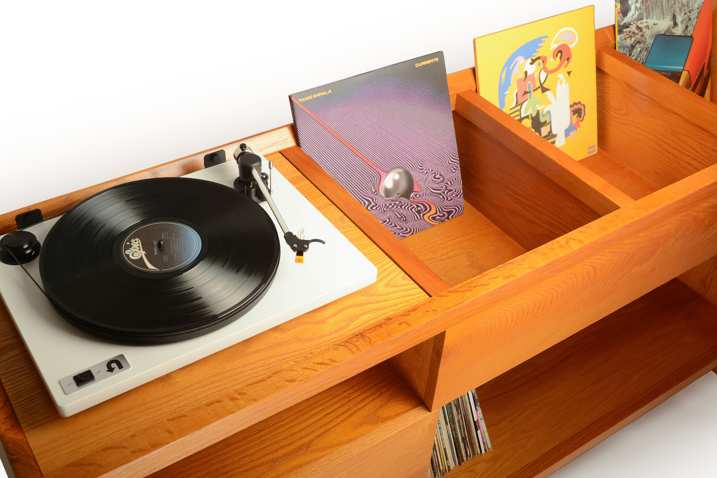 Turntable with black vinyl record on a wooden cabinet, with a wooden record crate holding colorful album covers.