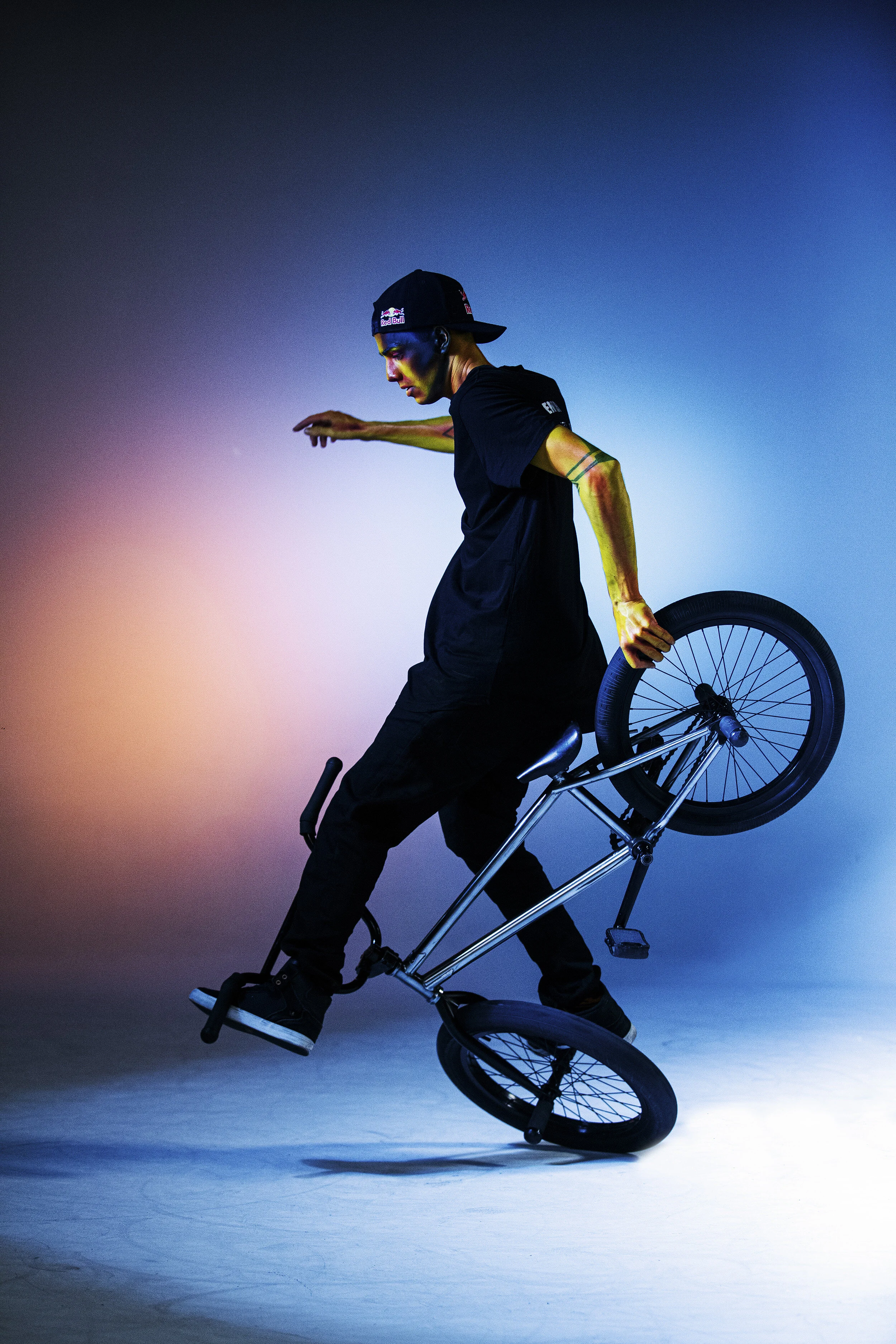 A young man performing a BMX stunt, balancing on the front wheel of his bike with a colorful, gradient background.