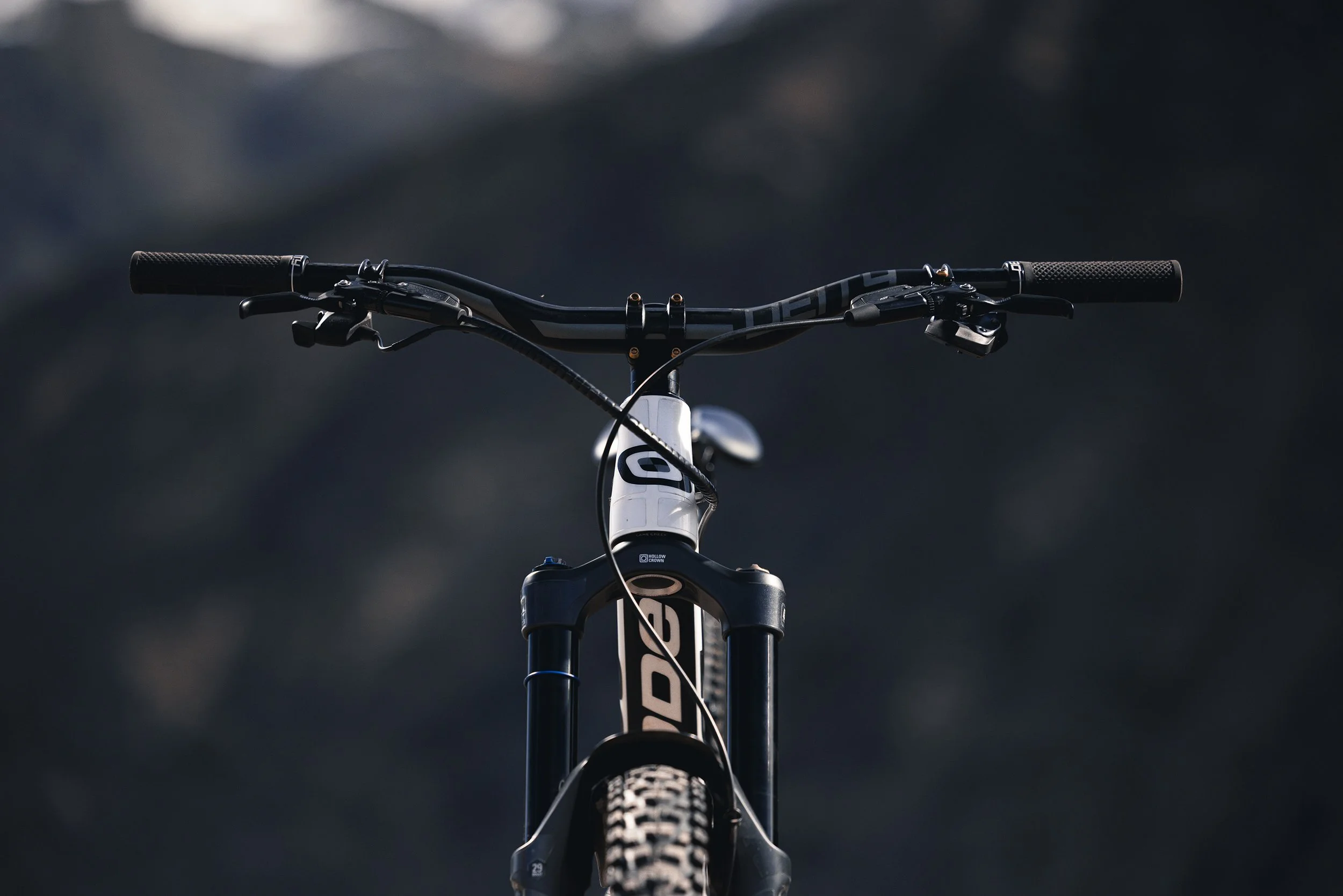 Front view of a black and white mountain bike, focusing on the handlebars, suspension fork, and front tire against a blurred dark background.