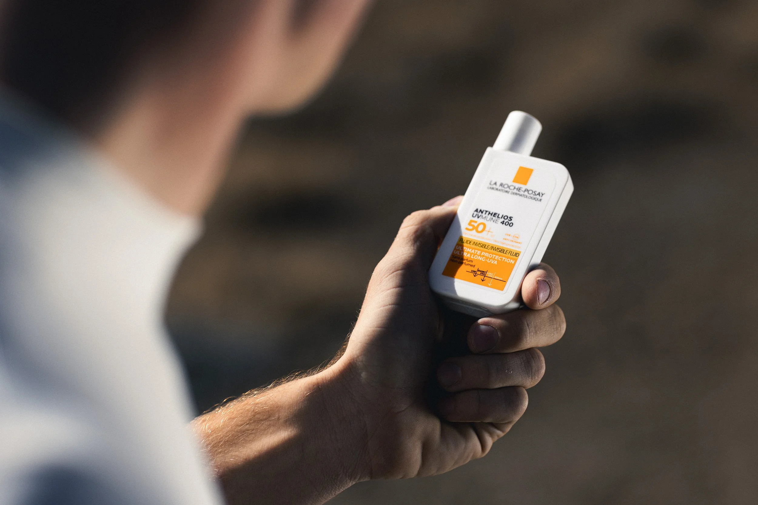 A person holding a bottle of La Roche-Posay Anthelios sunscreen with SPF 50+ outdoors.